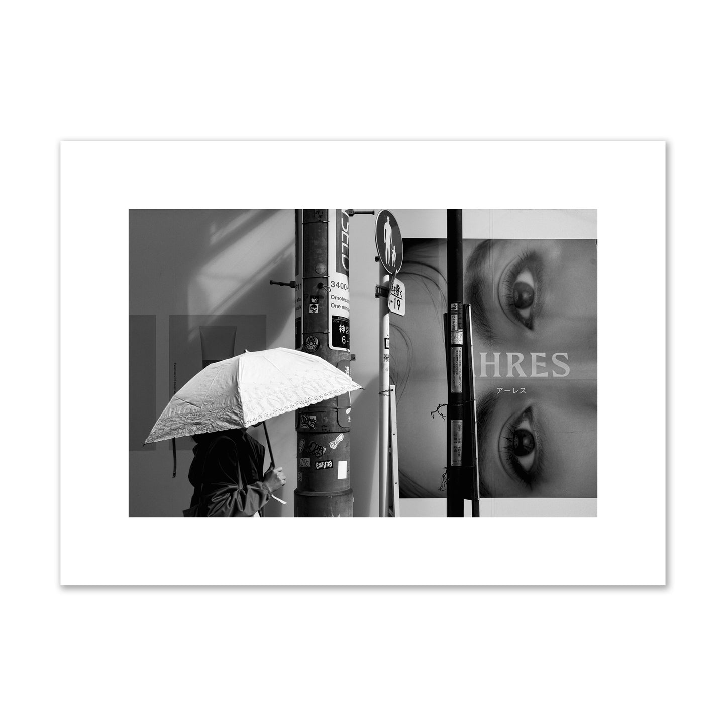 Fine art street photograph of a woman walking with an umbrella on a Tokyo street, passing beneath a billboard with two large eyes. Archival pigment print, medium size, unframed.