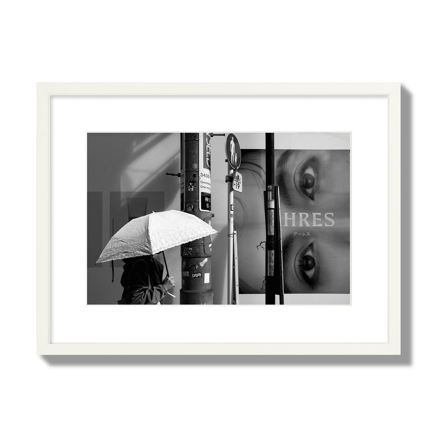 Fine art street photograph of a woman walking with an umbrella on a Tokyo street, passing beneath a billboard with two large eyes. Archival pigment print, medium size, white frame.