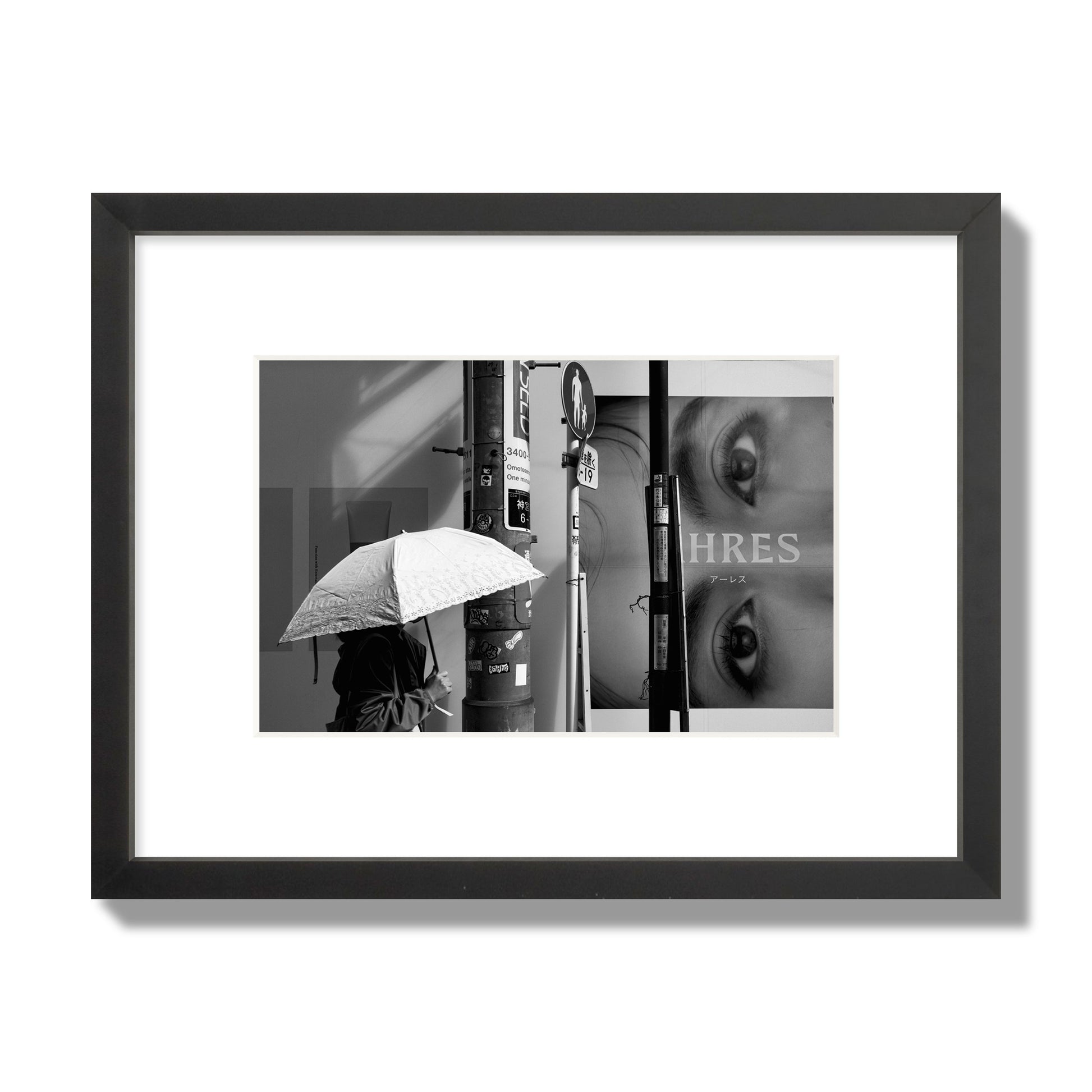Fine art street photograph of a woman walking with an umbrella on a Tokyo street, passing beneath a billboard with two large eyes. Archival pigment print, small size, black frame.