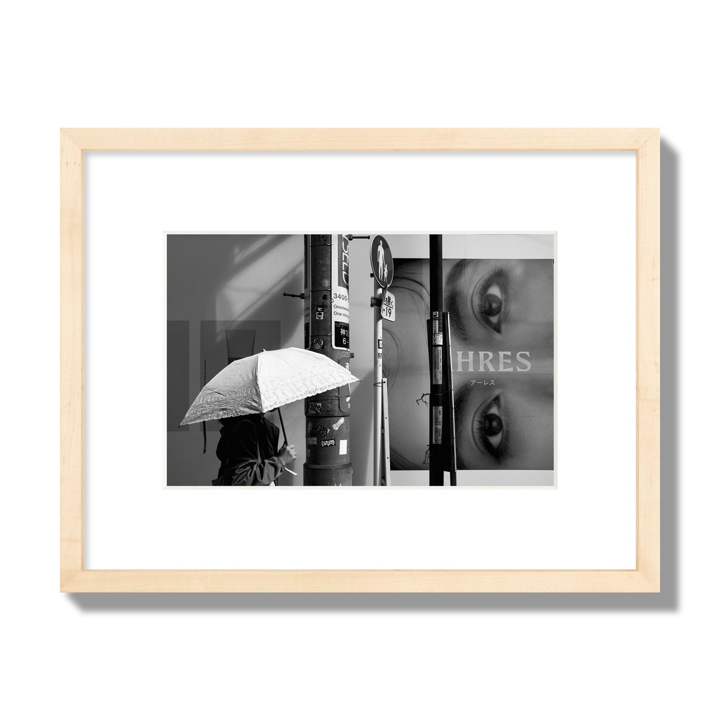 Fine art street photograph of a woman walking with an umbrella on a Tokyo street, passing beneath a billboard with two large eyes. Archival pigment print, small size, natural wood frame.