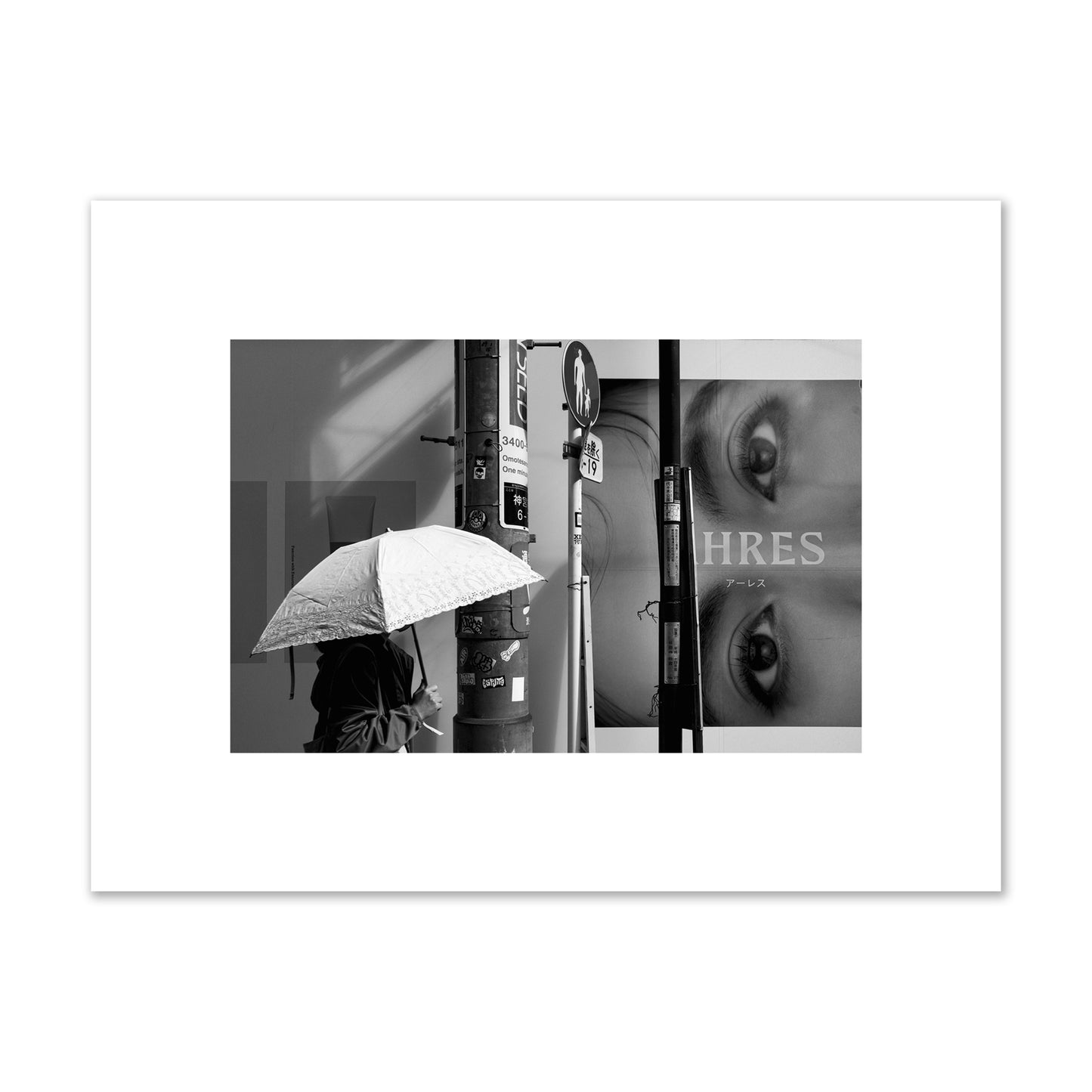 Fine art street photograph of a woman walking with an umbrella on a Tokyo street, passing beneath a billboard with two large eyes. Archival pigment print, small size, unframed.