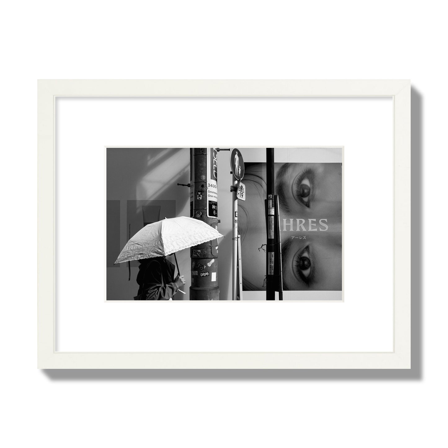 Fine art street photograph of a woman walking with an umbrella on a Tokyo street, passing beneath a billboard with two large eyes. Archival pigment print, small size, white frame.