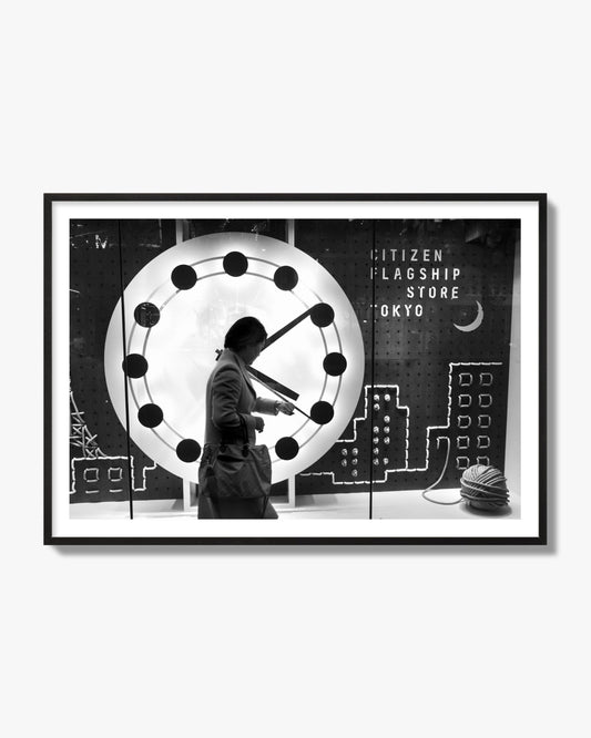 Fine art street photograph of a woman checking her watch as she walks past a giant clock on a busy Tokyo city street. Archival pigment print, black frame.