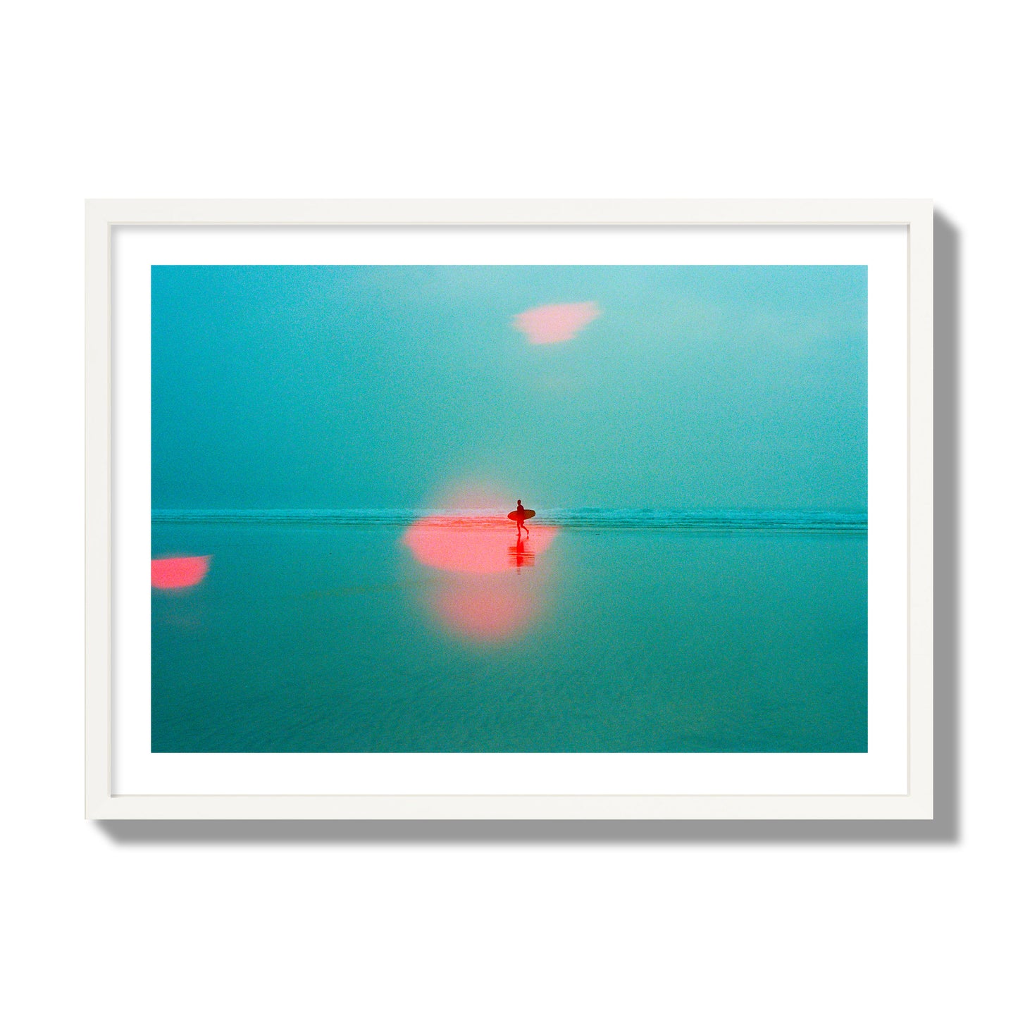 Fine art street photograph of a tranquil beach with a surfer running toward the waves, featuring a dreamlike composition with soft teal tones and a striking red lens flare. Archival pigment print, giant size, white frame.