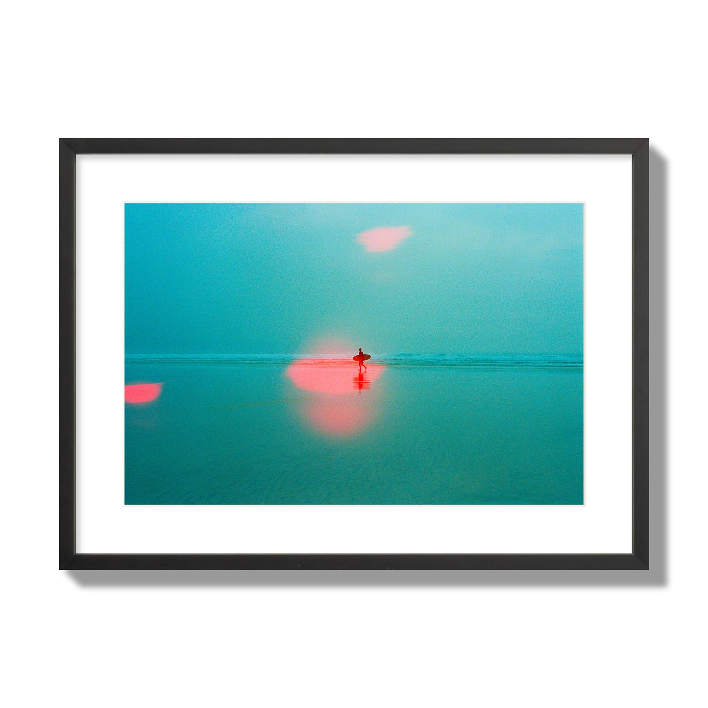 Fine art street photograph of a tranquil beach with a surfer running toward the waves, featuring a dreamlike composition with soft teal tones and a striking red lens flare. Archival pigment print, large size, black frame.