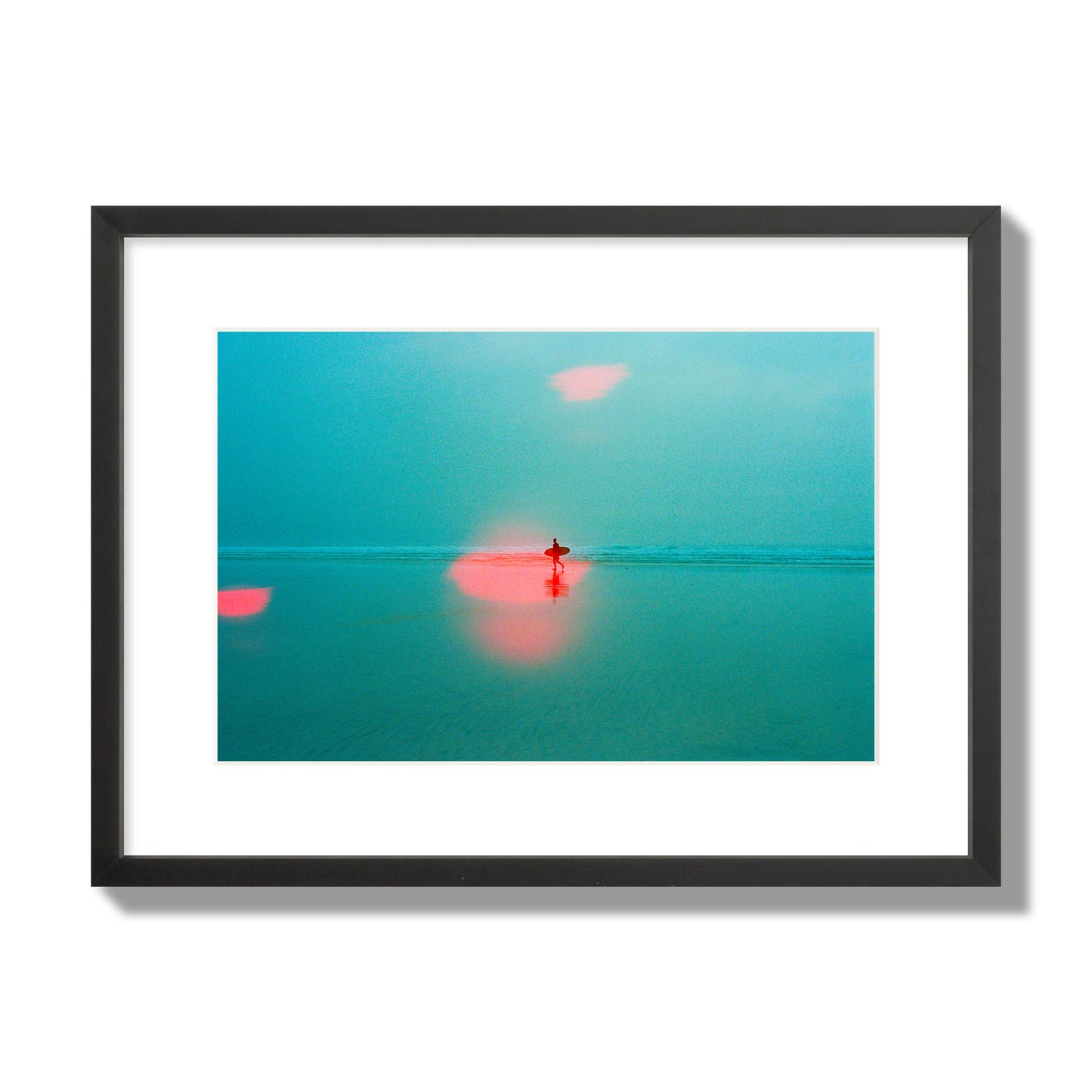 Fine art street photograph of a tranquil beach with a surfer running toward the waves, featuring a dreamlike composition with soft teal tones and a striking red lens flare. Archival pigment print, medium size, black frame.