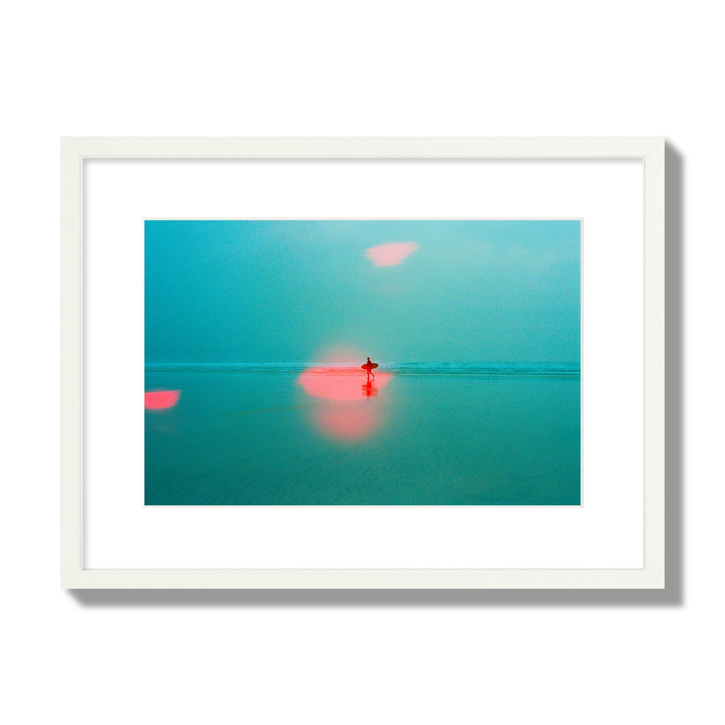 Fine art street photograph of a tranquil beach with a surfer running toward the waves, featuring a dreamlike composition with soft teal tones and a striking red lens flare. Archival pigment print, medium size, white frame.