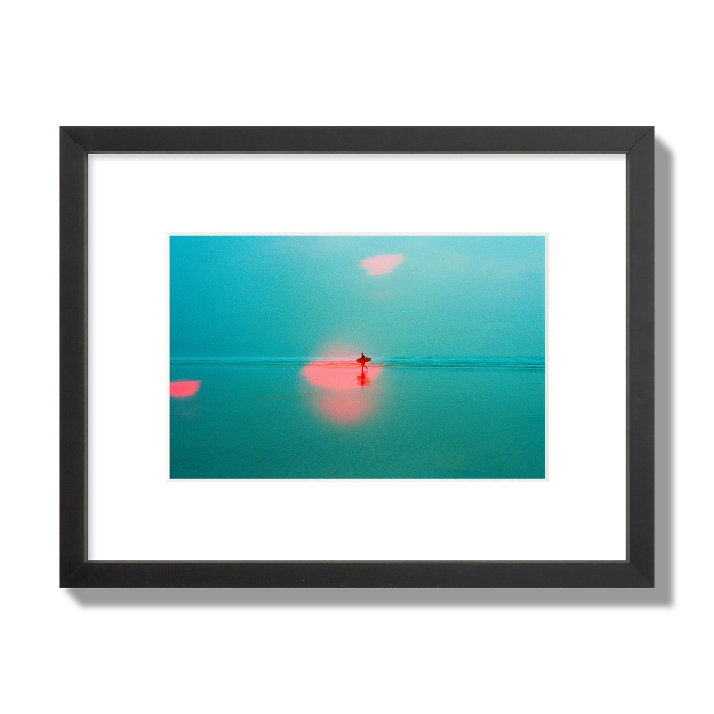 Fine art street photograph of a tranquil beach with a surfer running toward the waves, featuring a dreamlike composition with soft teal tones and a striking red lens flare. Archival pigment print, small size, black frame.