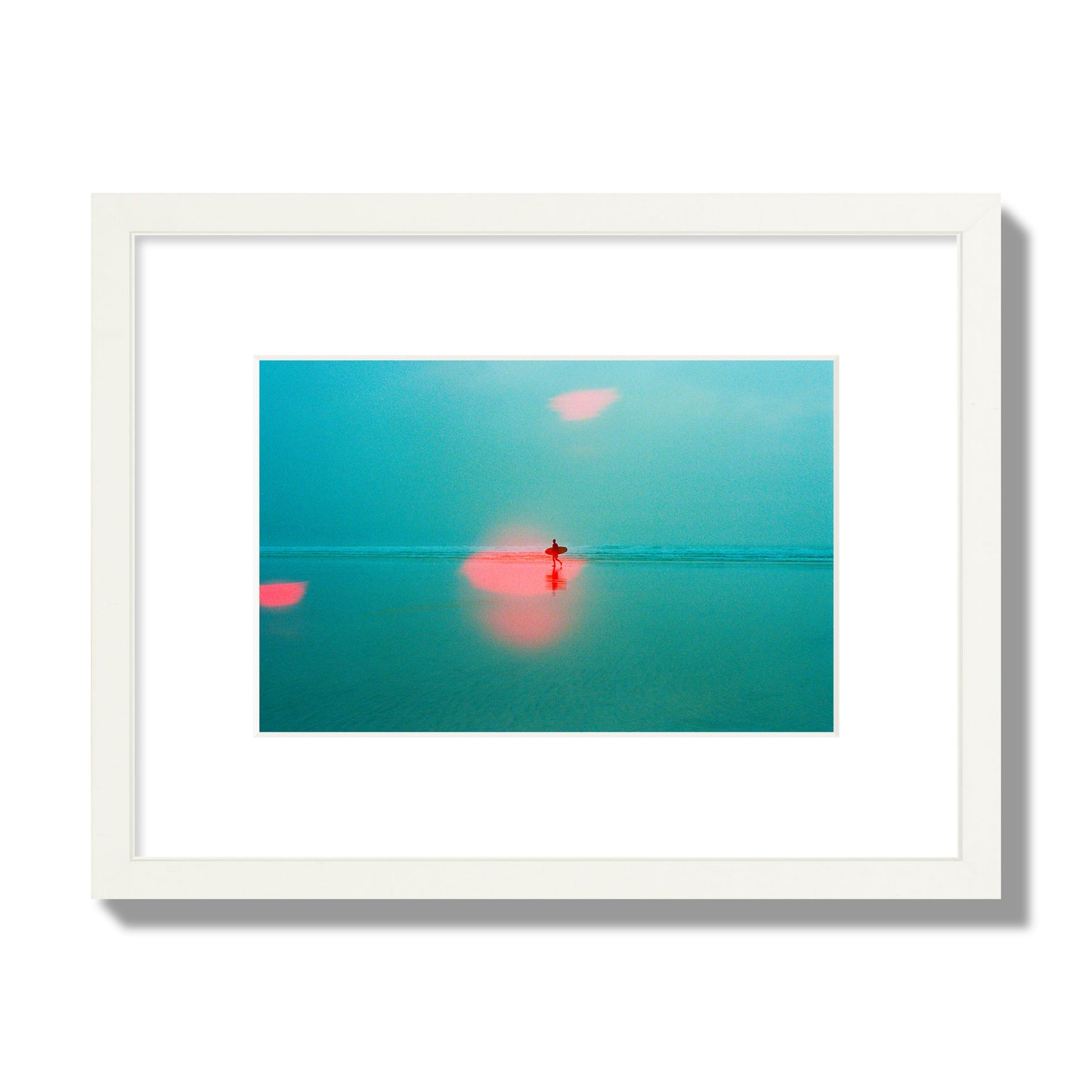 Fine art street photograph of a tranquil beach with a surfer running toward the waves, featuring a dreamlike composition with soft teal tones and a striking red lens flare. Archival pigment print, small size, white frame.