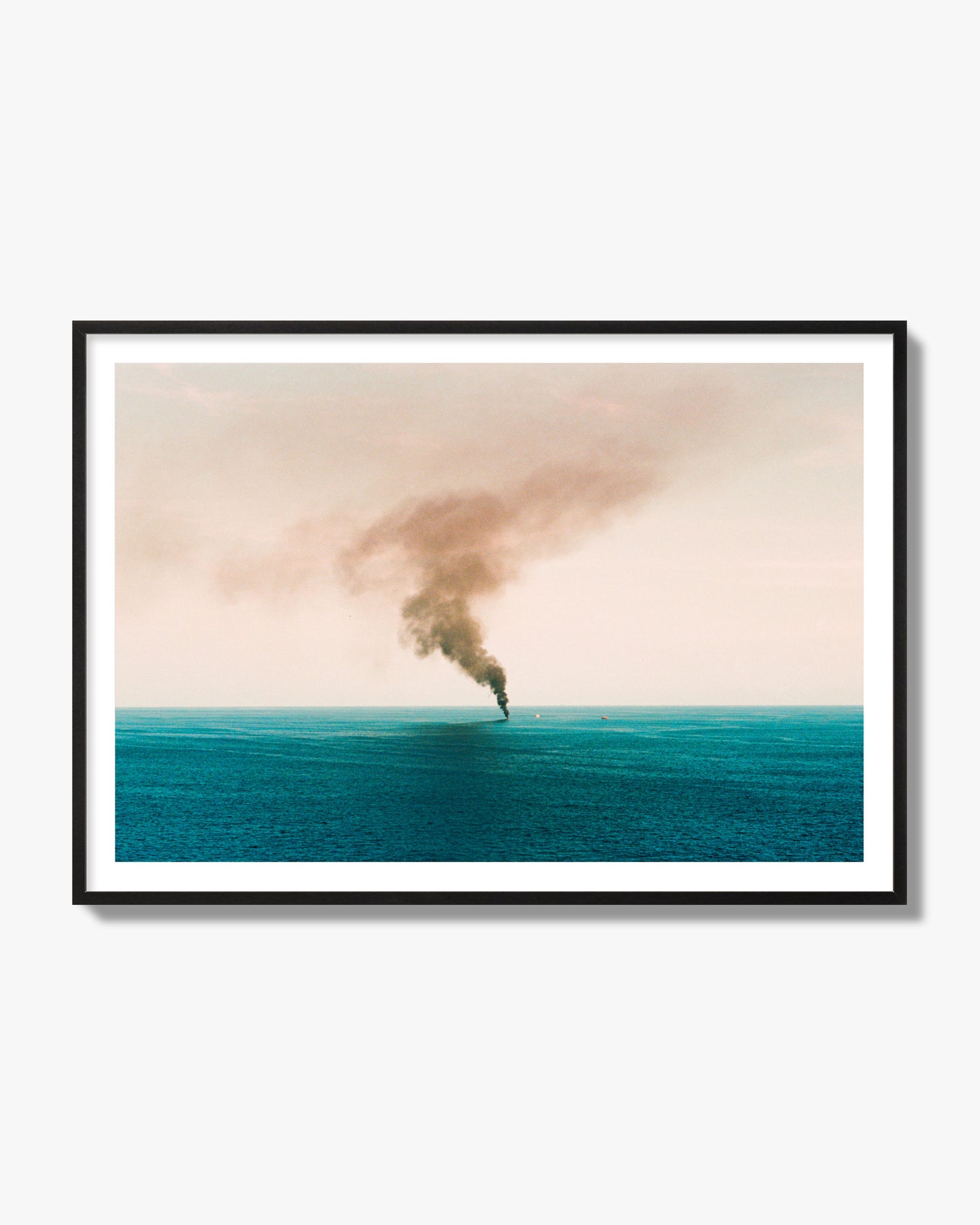 Fine art street photograph of a moody seascape with smoke rising from a distant boat, capturing a sense of mystery and atmosphere. Archival pigment print, black frame.