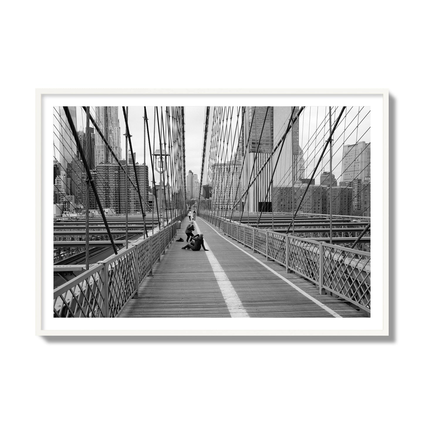 Fine art black and white photograph of a person posing on the Brooklyn Bridge with the cityscape in the background, archival pigment print, collector size, white frame