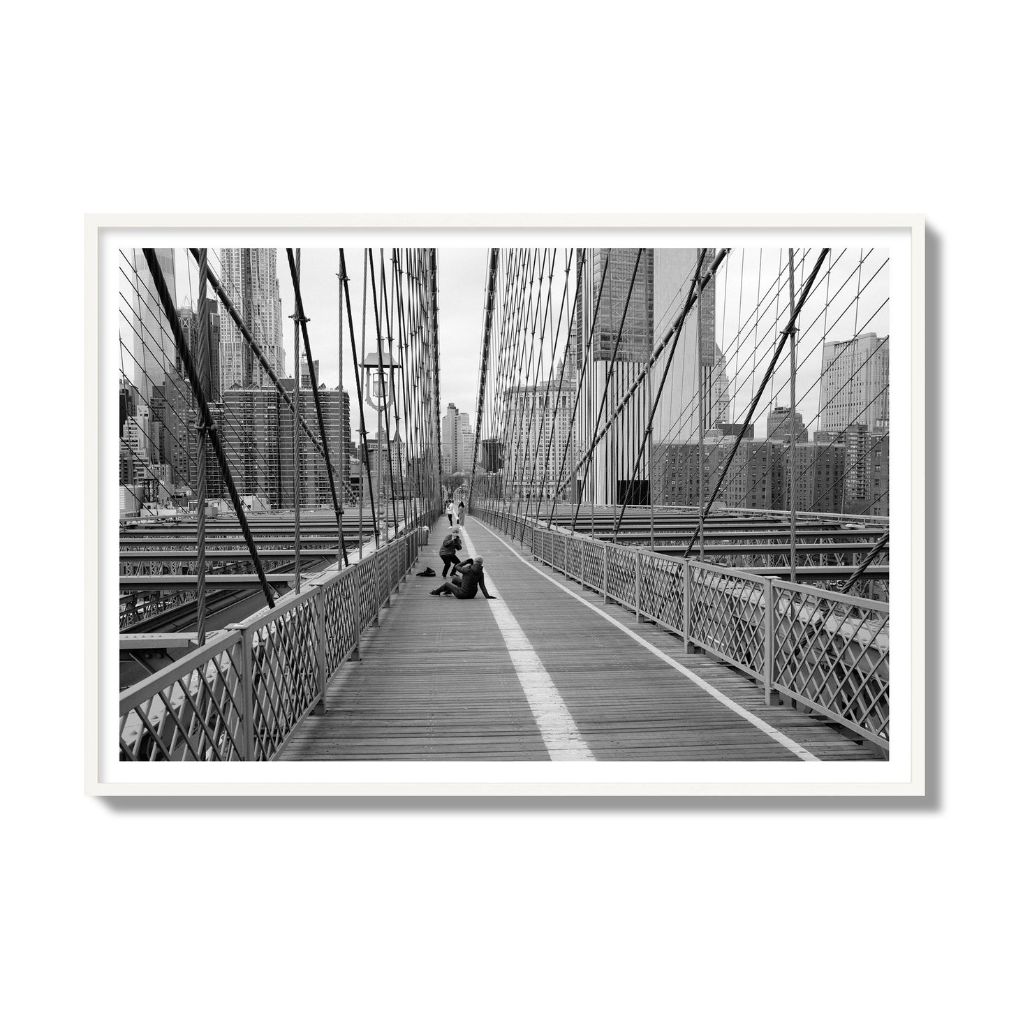 Fine art black and white photograph of a person posing on the Brooklyn Bridge with the cityscape in the background, archival pigment print, gallery size, white frame