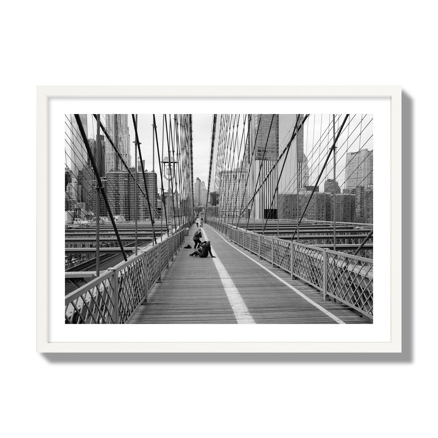 Fine art black and white photograph of a person posing on the Brooklyn Bridge with the cityscape in the background, archival pigment print, giant size, white frame