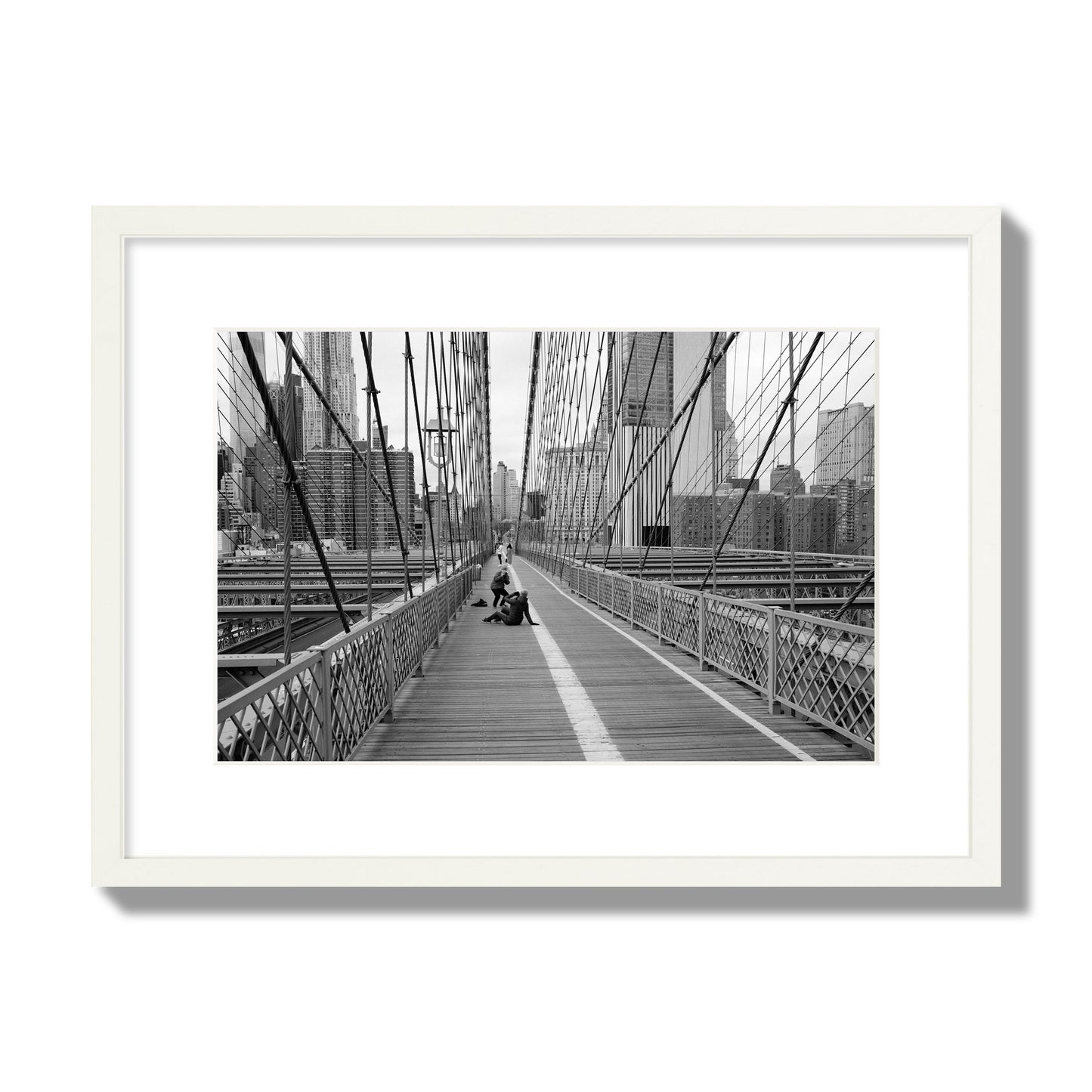 Fine art black and white photograph of a person posing on the Brooklyn Bridge with the cityscape in the background, archival pigment print, medium size, white frame