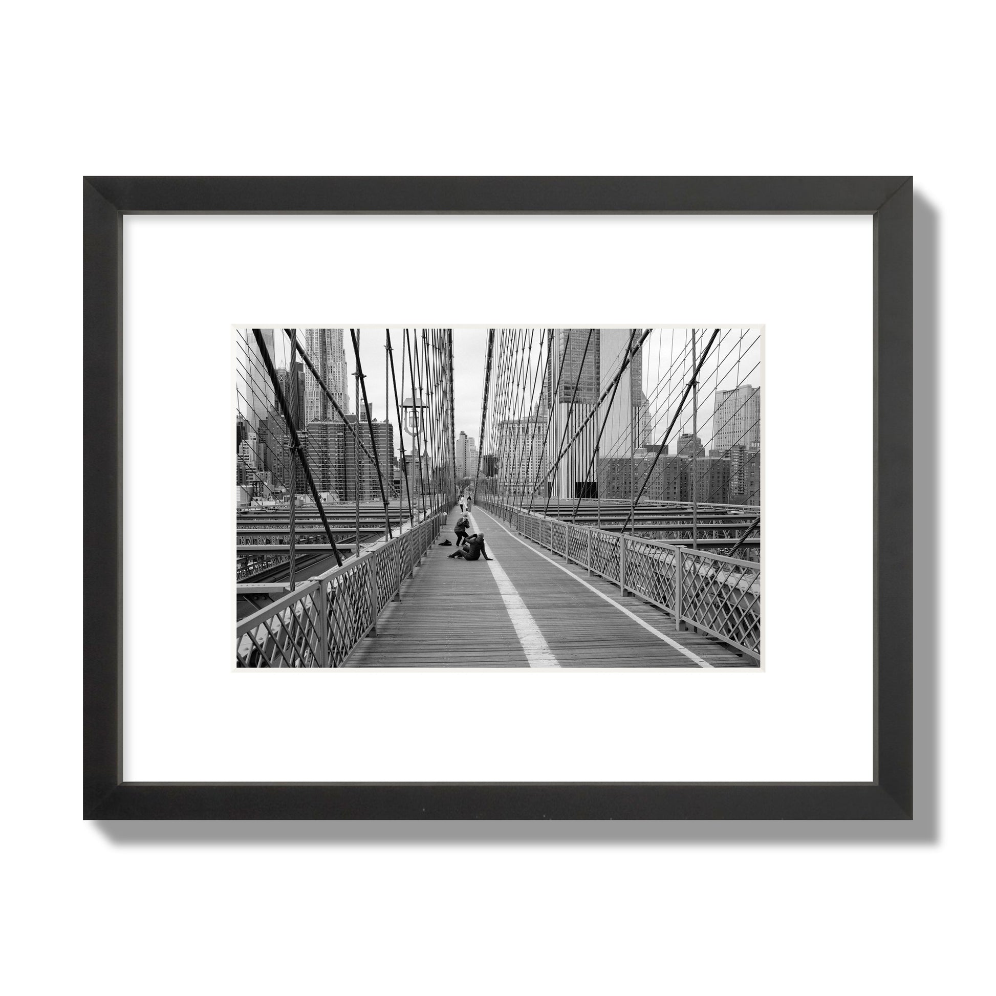 Fine art black and white photograph of a person posing on the Brooklyn Bridge with the cityscape in the background, archival pigment print, small size, black frame