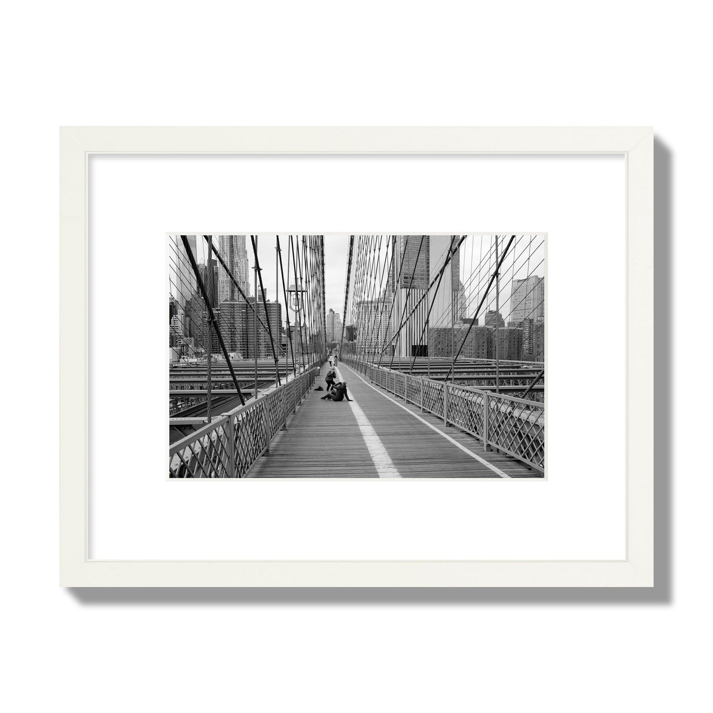 Fine art black and white photograph of a person posing on the Brooklyn Bridge with the cityscape in the background, archival pigment print, small size, white frame