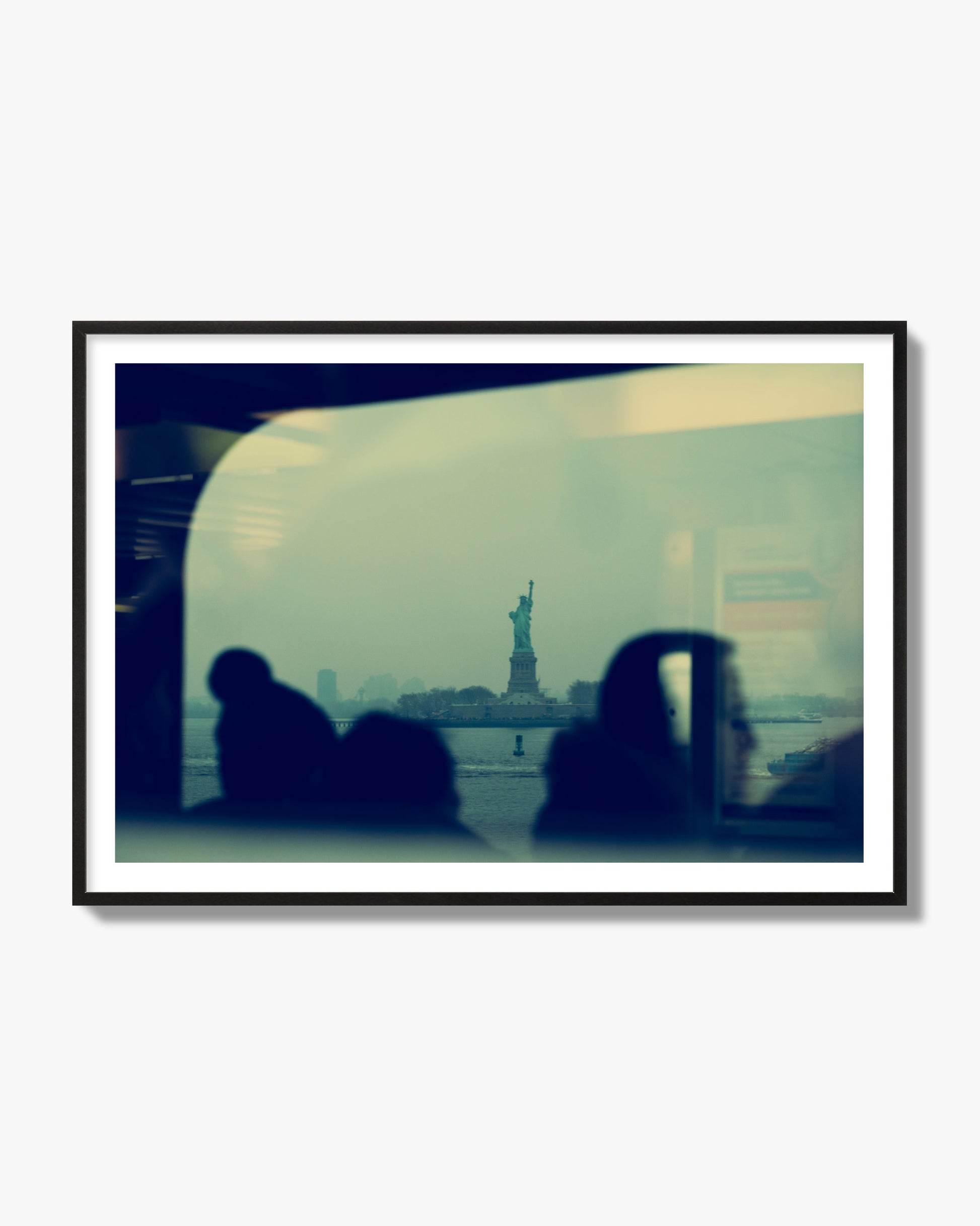 Fine art photograph of passengers silhouetted on a crowded ferry with the Statue of Liberty in the background, archival pigment print, black frame.