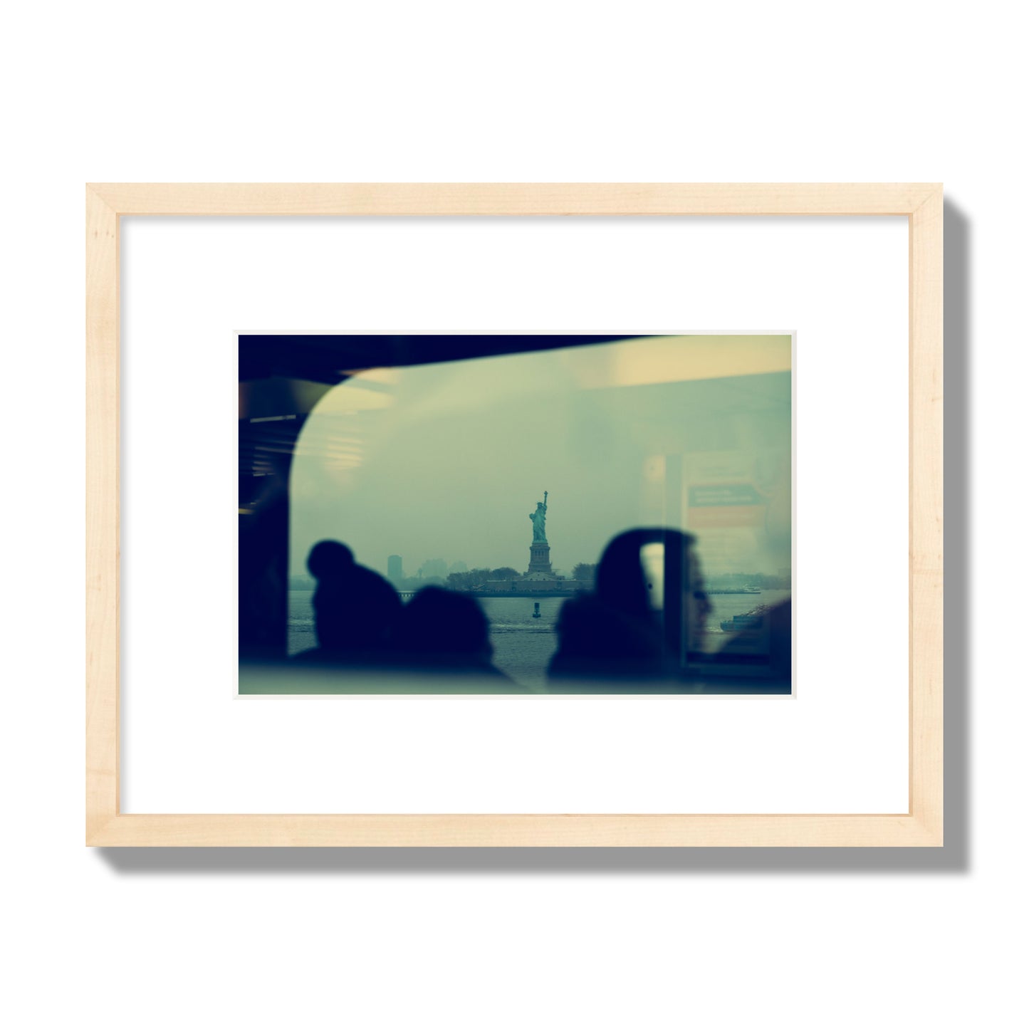 Fine art photograph of passengers silhouetted on a crowded ferry with the Statue of Liberty in the background, archival pigment print, small size, natural wood frame.