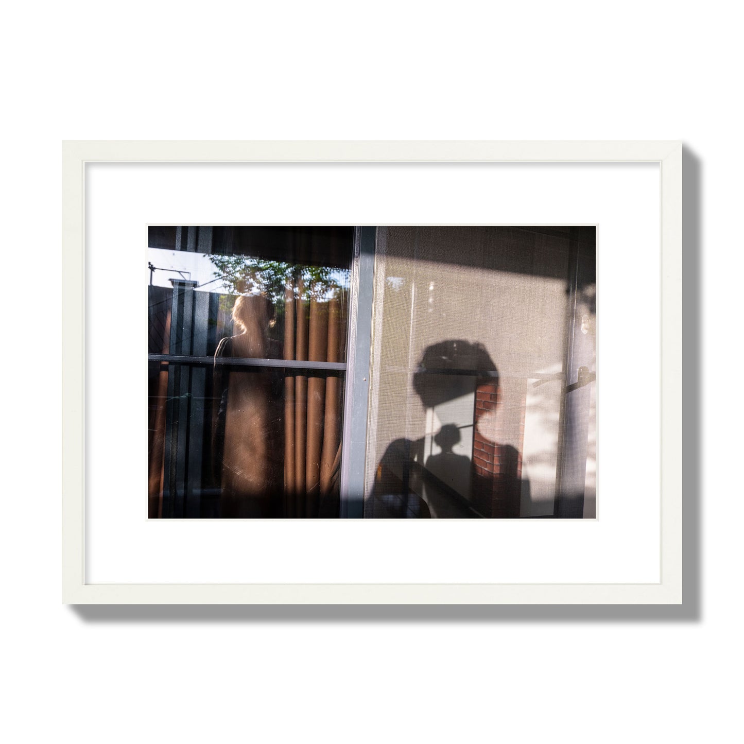 Fine art photograph of a person's silhouette against a window with curtains, archival pigment print, medium size, white frame.