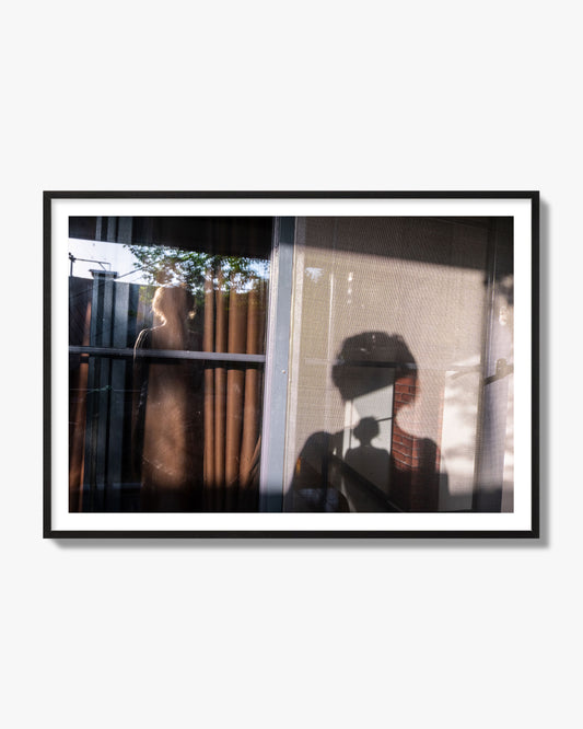 Fine art photograph of a person's silhouette against a window with curtains, archival pigment print, black frame.