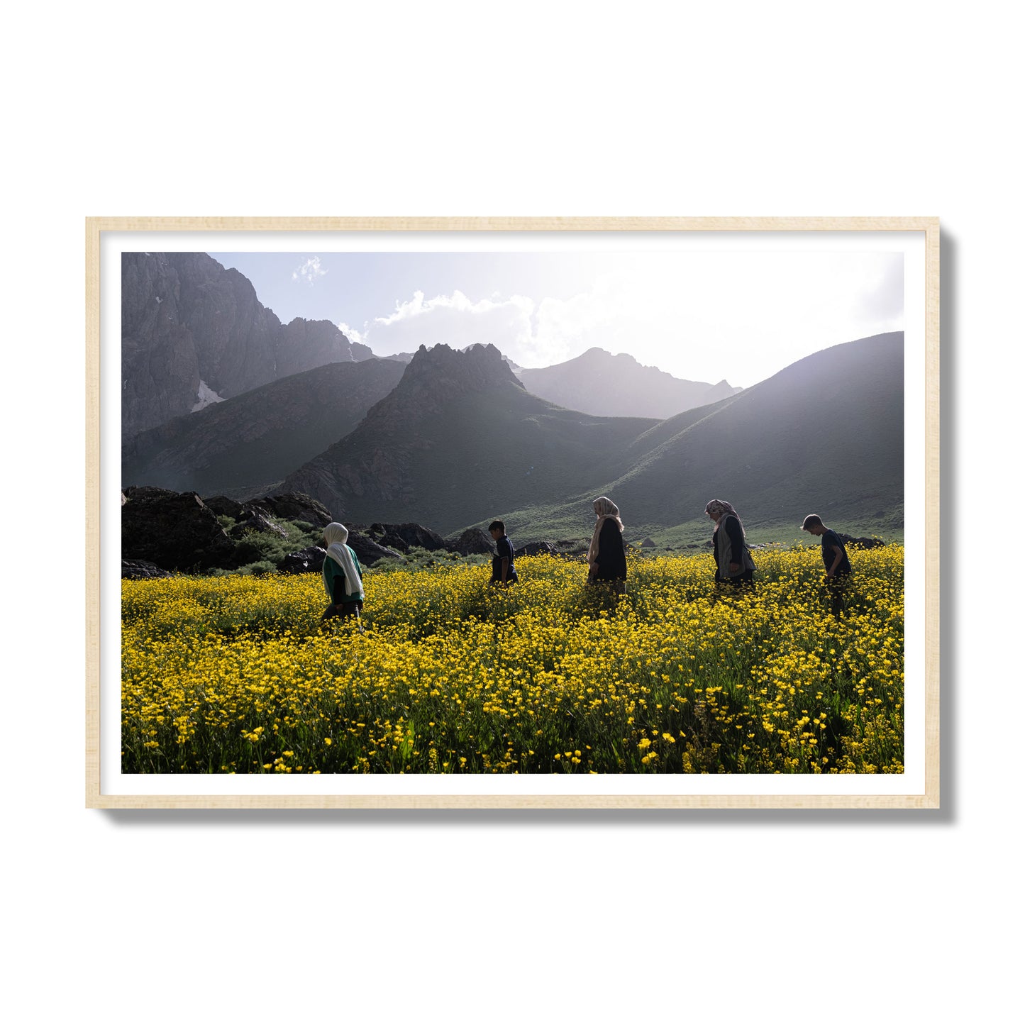 Fine art photograph of people walking through a field of yellow flowers with mountains in the background, archival pigment print, gallery size, natural wood frame.