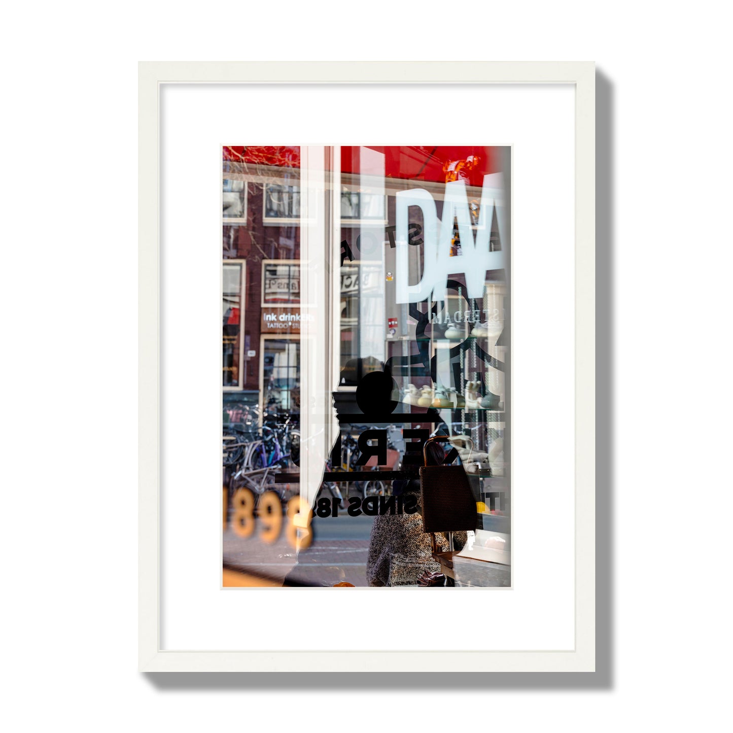 Fine art street photograph of a busy Amsterdam street scene with reflections, silhouettes, shoppers, and store signs. Archival pigment print, medium size, white frame.