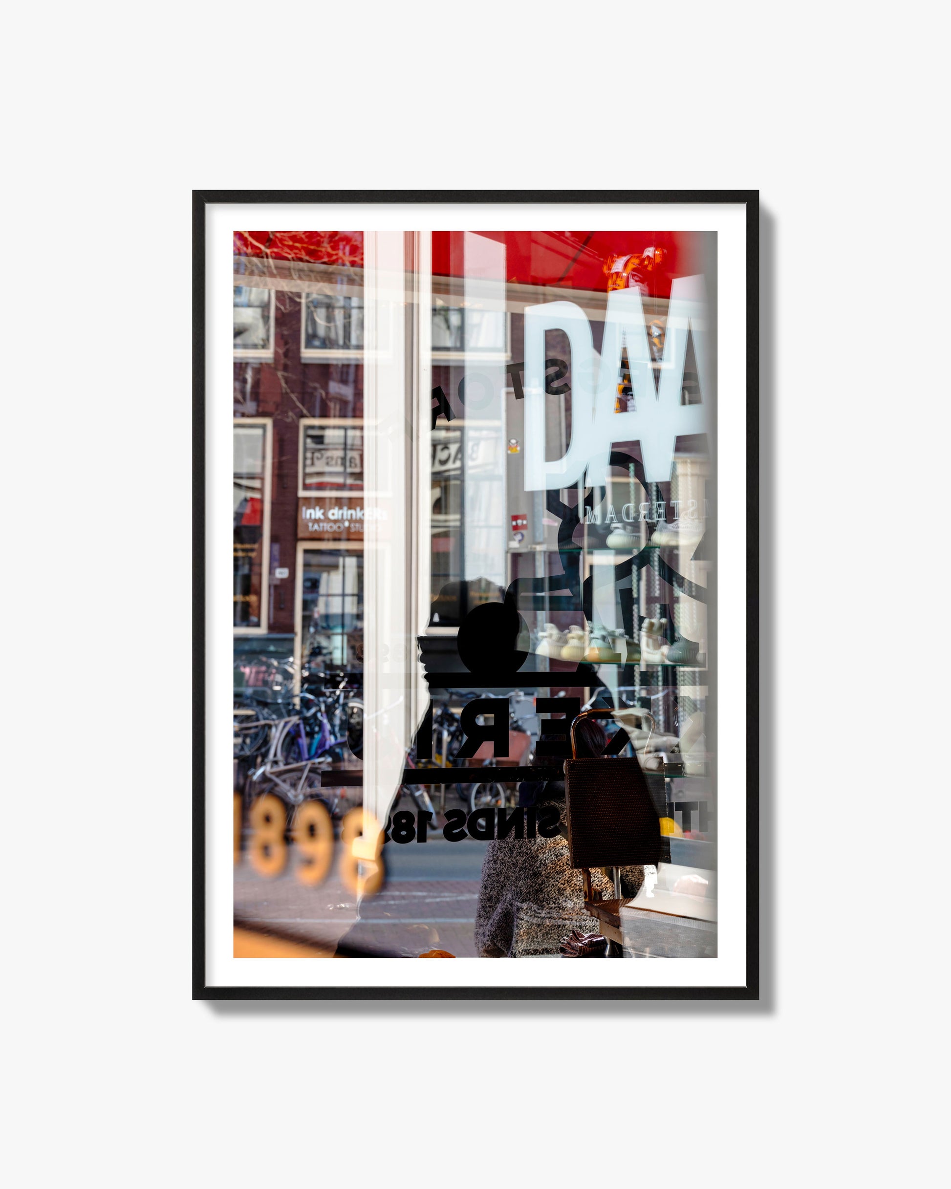 Fine art street photograph of a busy Amsterdam street scene with reflections, silhouettes, shoppers, and store signs. Archival pigment print, black frame.