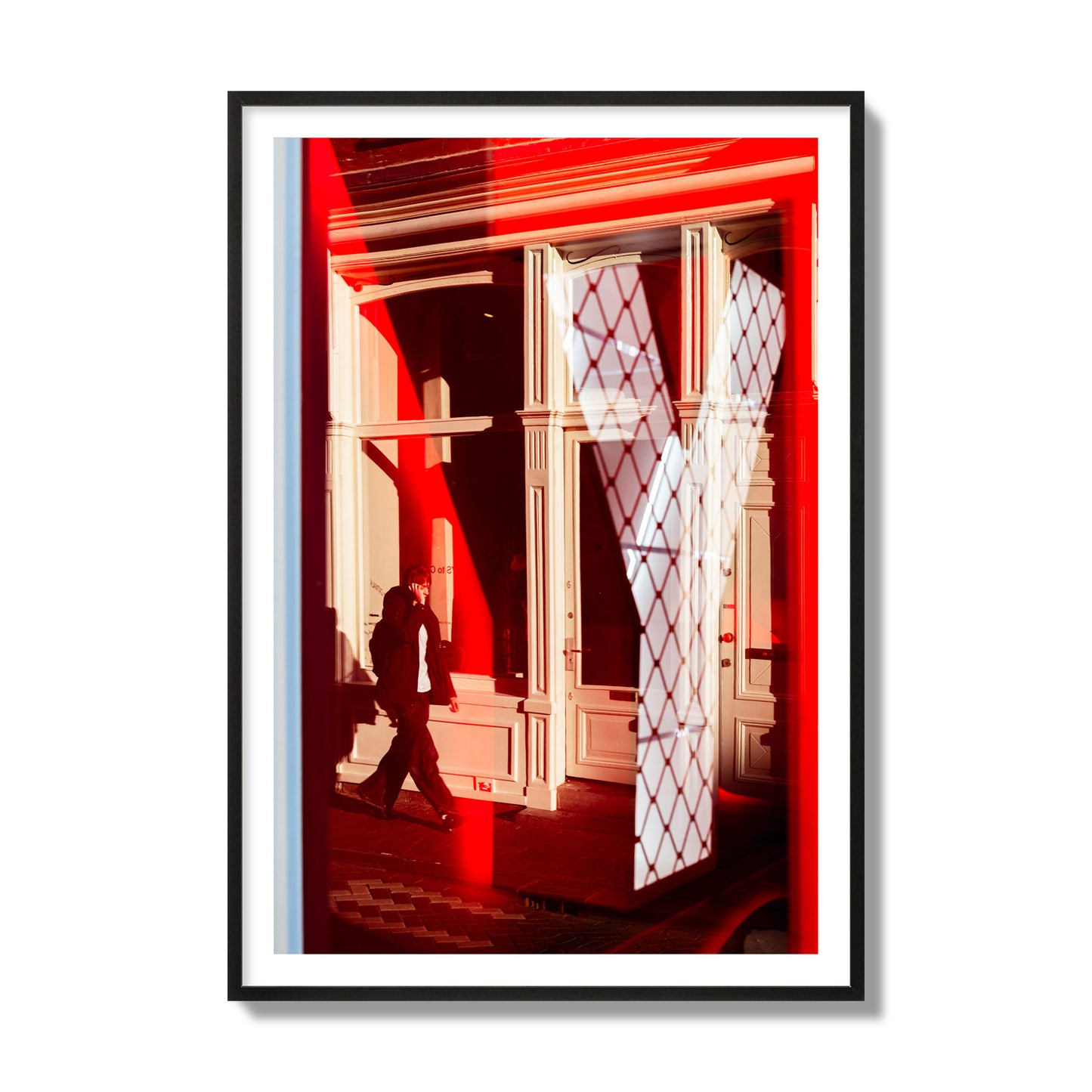 Fine art street photograph of an Amsterdam street scene showing bright red and white reflections of a large letter Y, a man walking, and multiple store fronts. Archival pigment print, collector size, black frame.