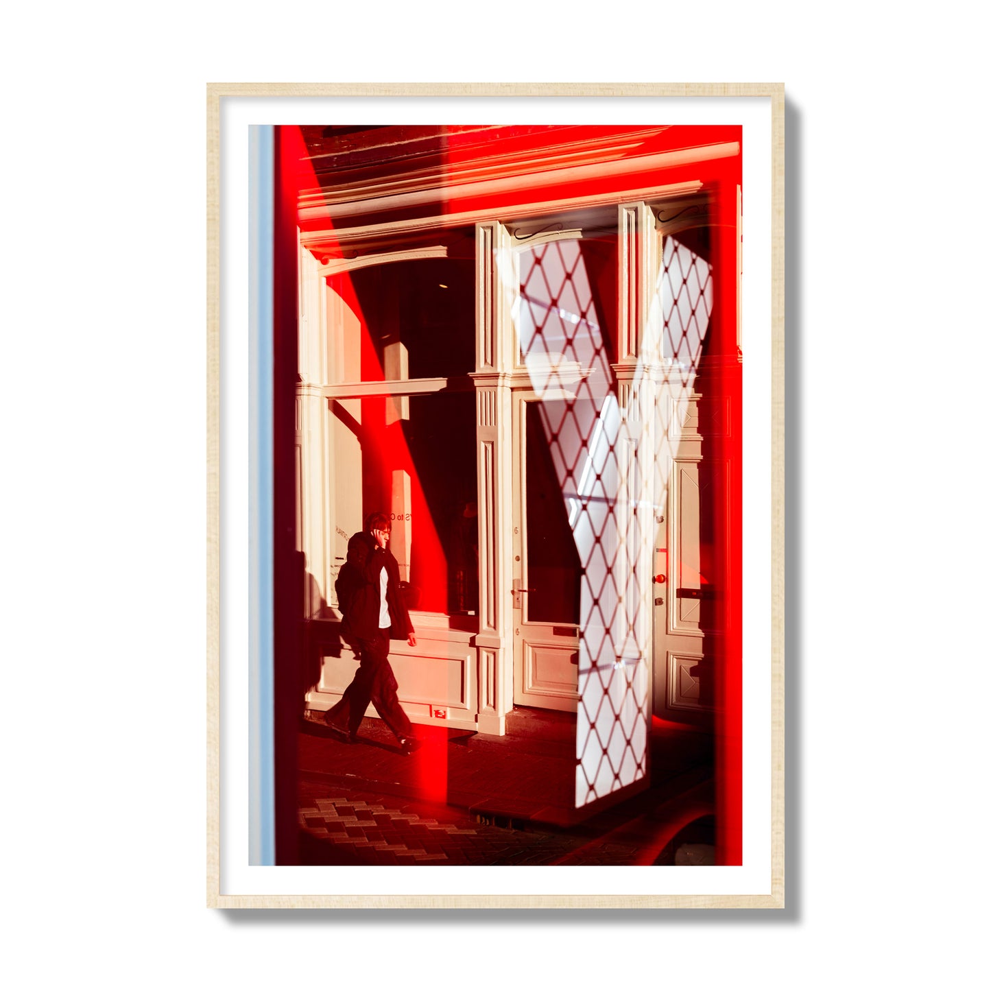 Fine art street photograph of an Amsterdam street scene showing bright red and white reflections of a large letter Y, a man walking, and multiple store fronts. Archival pigment print, collector size, natural wood frame.