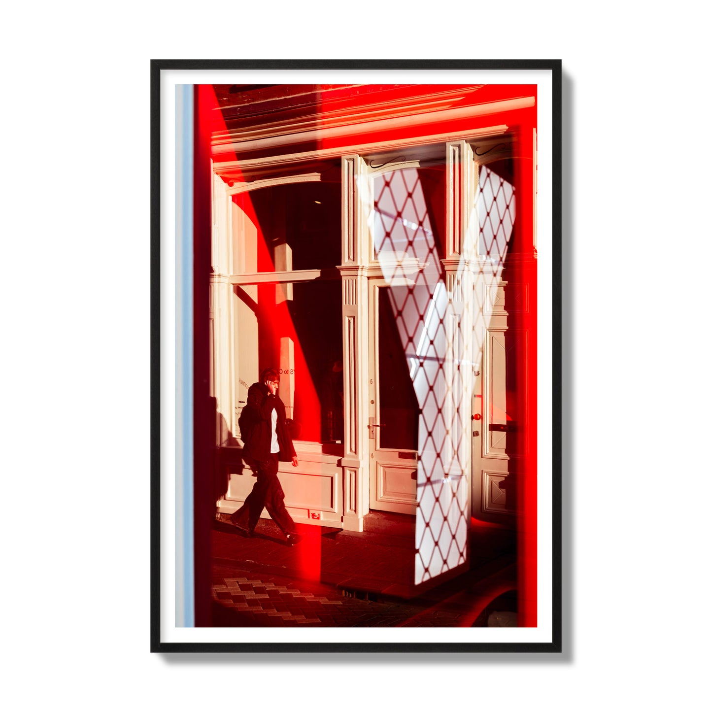 Fine art street photograph of an Amsterdam street scene showing bright red and white reflections of a large letter Y, a man walking, and multiple store fronts. Archival pigment print, gallery size, black frame.