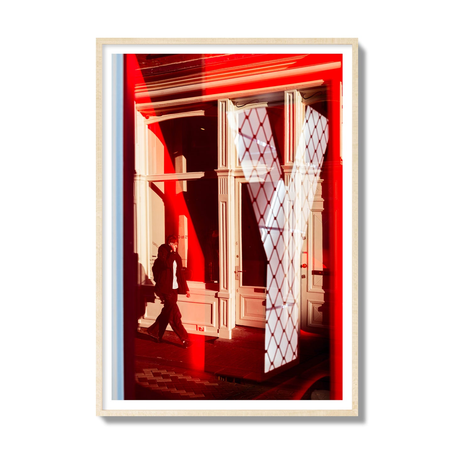 Fine art street photograph of an Amsterdam street scene showing bright red and white reflections of a large letter Y, a man walking, and multiple store fronts. Archival pigment print, gallery size, natural wood frame.