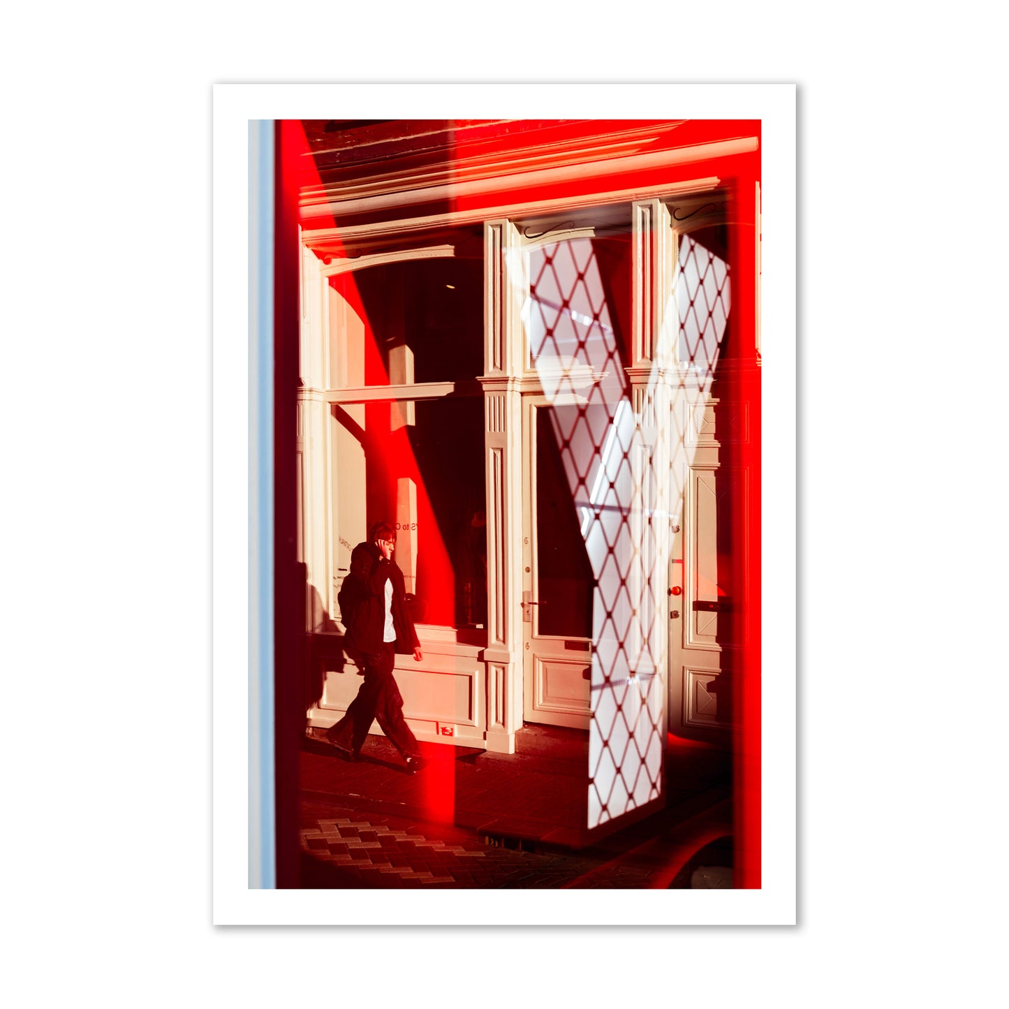 Fine art street photograph of an Amsterdam street scene showing bright red and white reflections of a large letter Y, a man walking, and multiple store fronts. Archival pigment print, gallery size, unframed.
