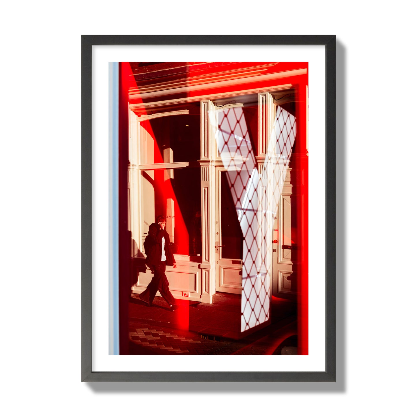 Fine art street photograph of an Amsterdam street scene showing bright red and white reflections of a large letter Y, a man walking, and multiple store fronts. Archival pigment print, giant size, black frame.