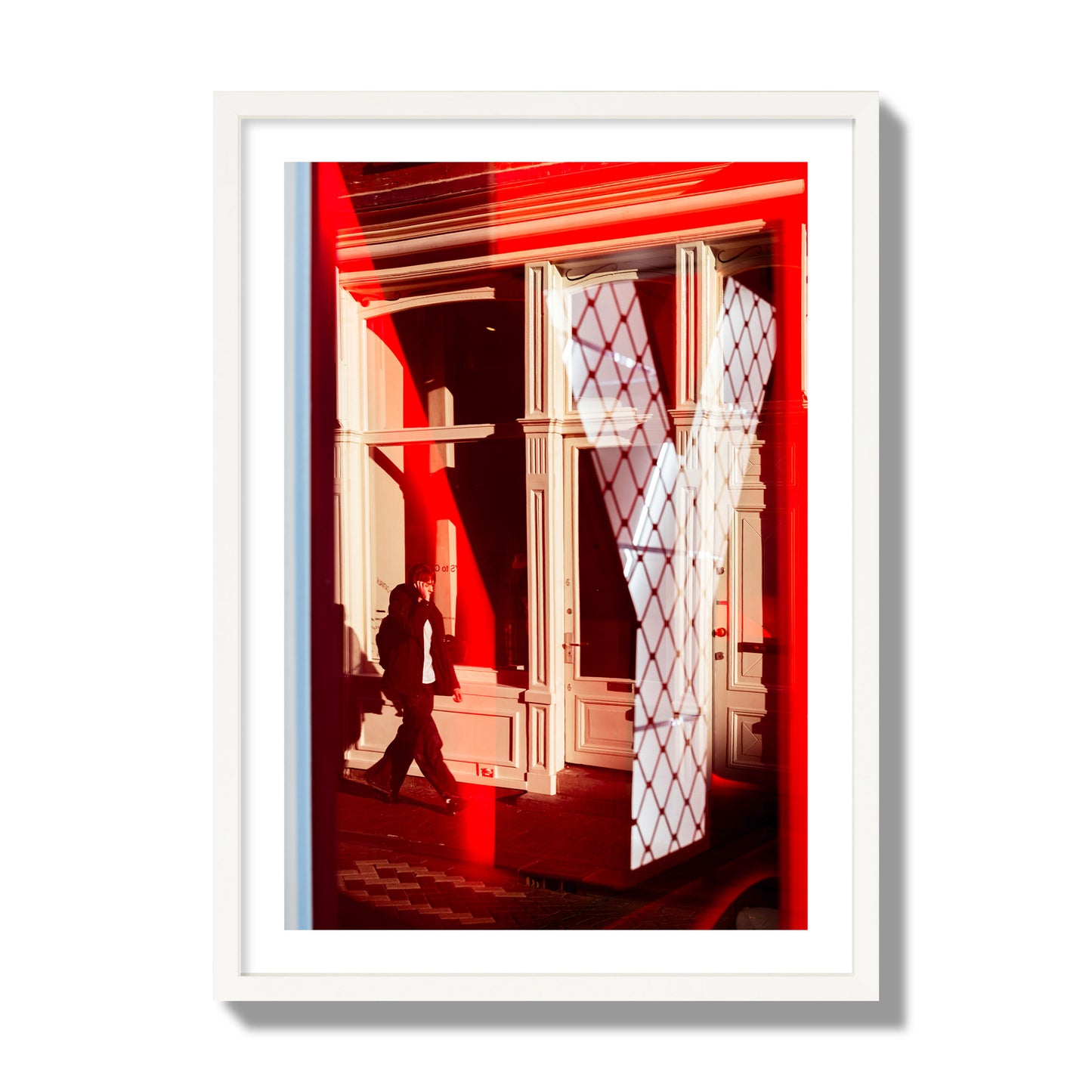 Fine art street photograph of an Amsterdam street scene showing bright red and white reflections of a large letter Y, a man walking, and multiple store fronts. Archival pigment print, giant size, white frame.