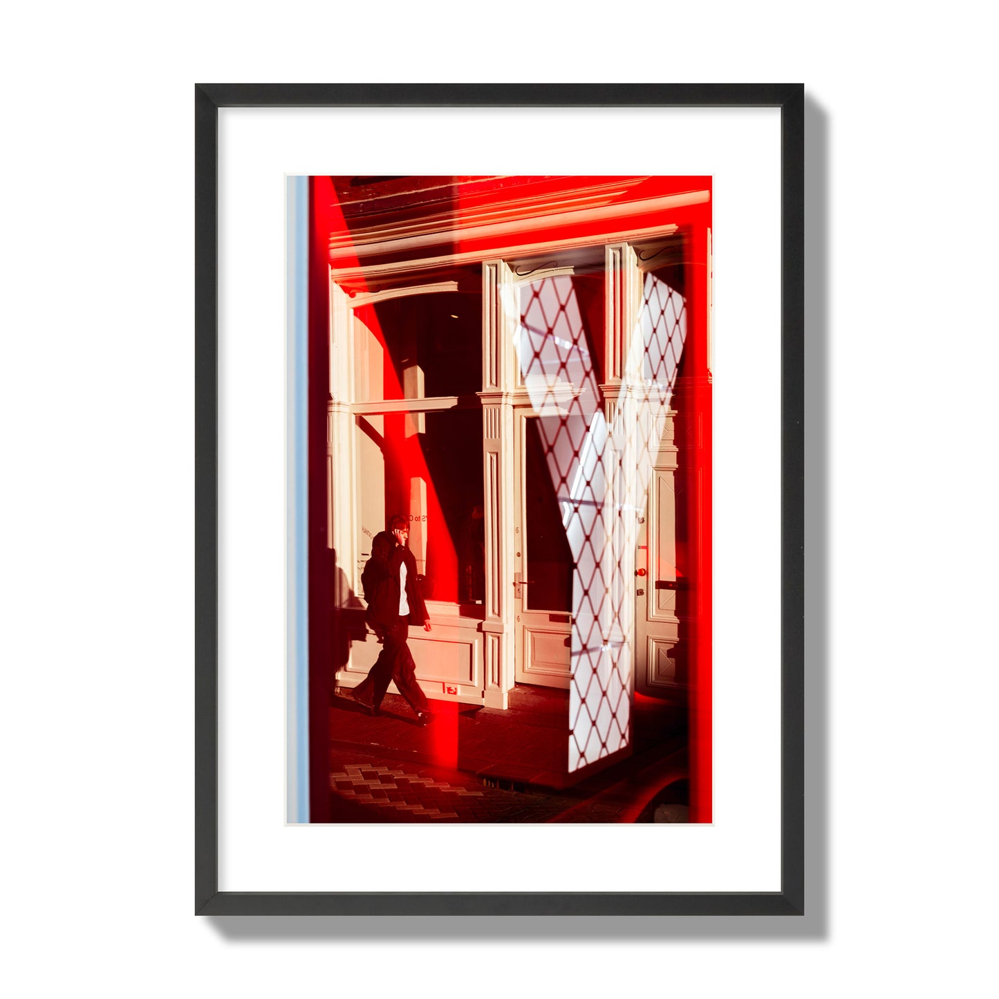 Fine art street photograph of an Amsterdam street scene showing bright red and white reflections of a large letter Y, a man walking, and multiple store fronts. Archival pigment print, large size, black frame.
