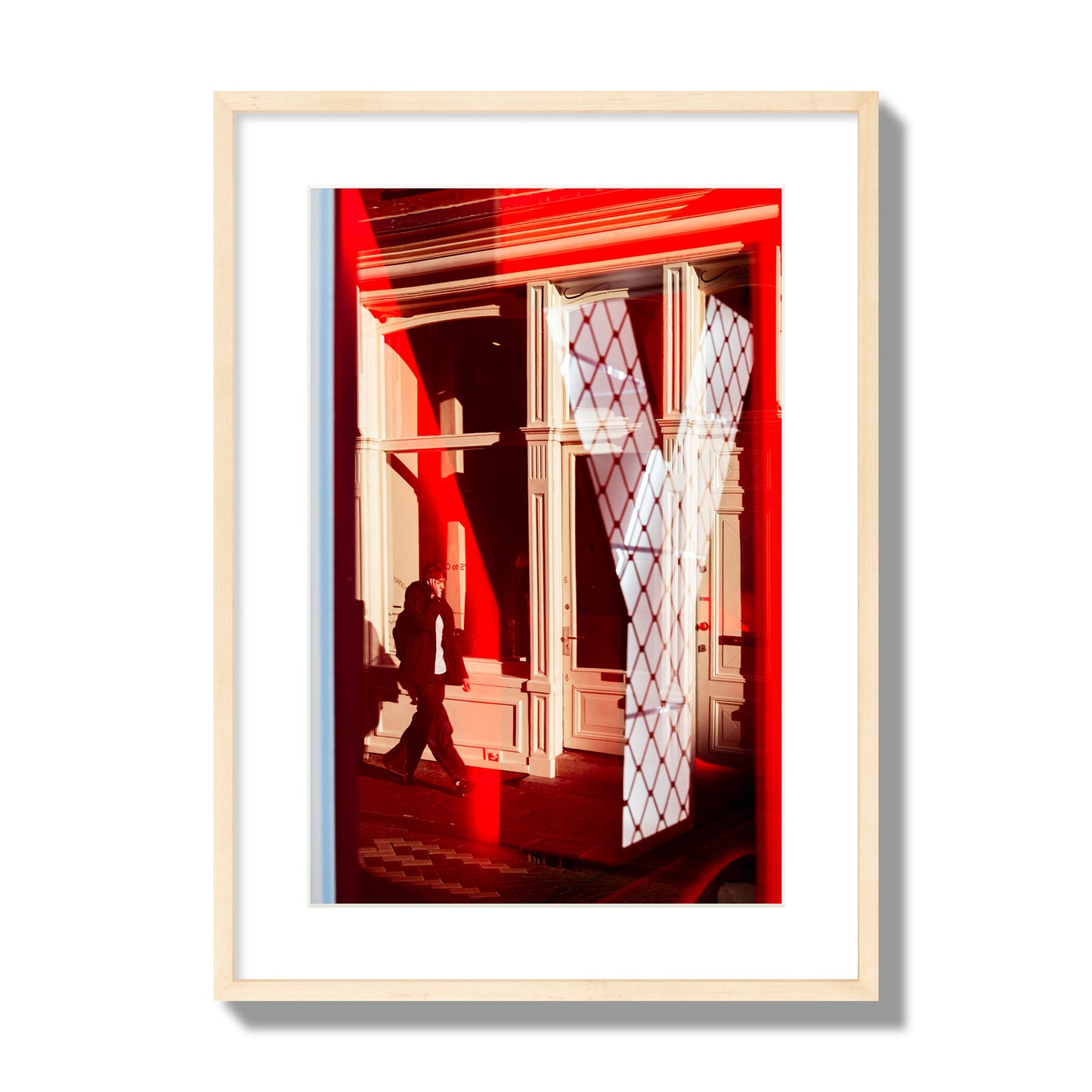 Fine art street photograph of an Amsterdam street scene showing bright red and white reflections of a large letter Y, a man walking, and multiple store fronts. Archival pigment print, large size, natural wood frame.