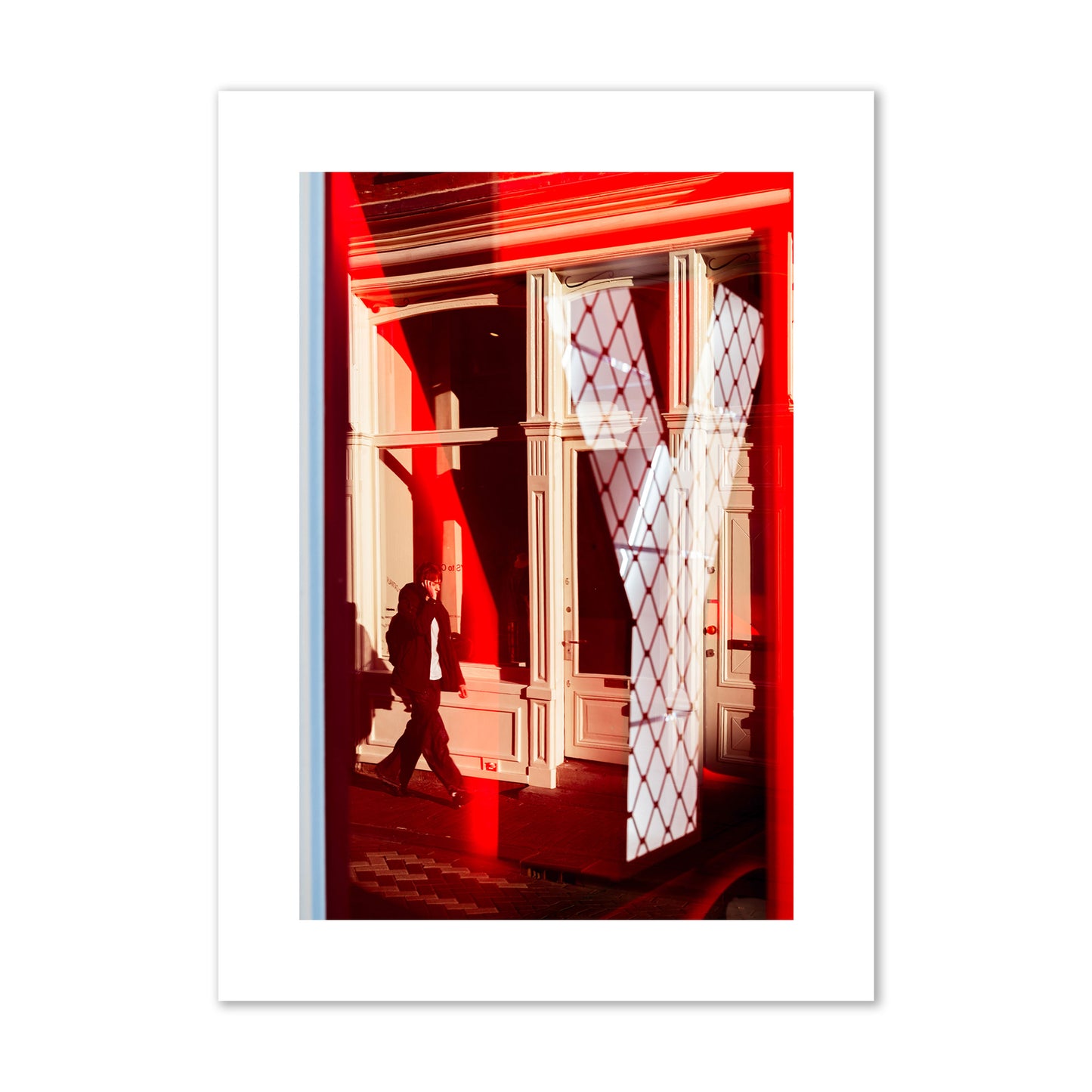 Fine art street photograph of an Amsterdam street scene showing bright red and white reflections of a large letter Y, a man walking, and multiple store fronts. Archival pigment print, large size, unframed.