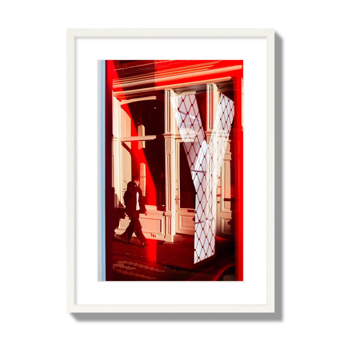 Fine art street photograph of an Amsterdam street scene showing bright red and white reflections of a large letter Y, a man walking, and multiple store fronts. Archival pigment print, large size, white frame.