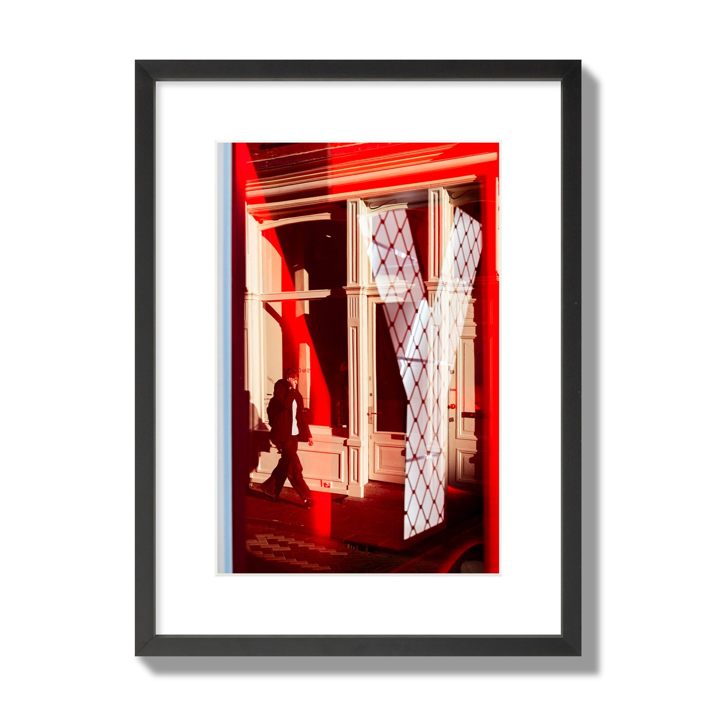 Fine art street photograph of an Amsterdam street scene showing bright red and white reflections of a large letter Y, a man walking, and multiple store fronts. Archival pigment print, medium size, black frame.