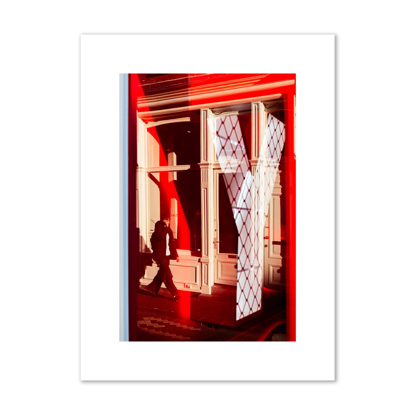 Fine art street photograph of an Amsterdam street scene showing bright red and white reflections of a large letter Y, a man walking, and multiple store fronts. Archival pigment print, medium size, unframed.