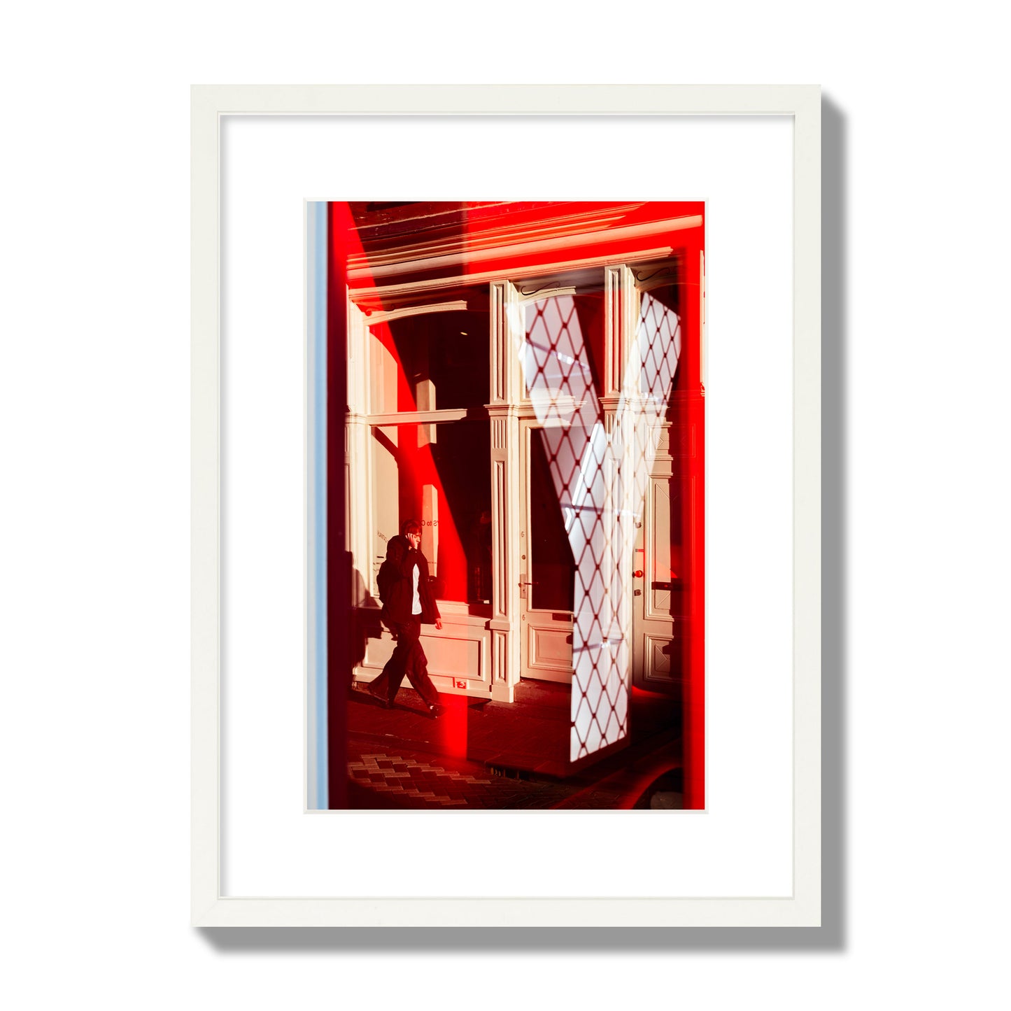 Fine art street photograph of an Amsterdam street scene showing bright red and white reflections of a large letter Y, a man walking, and multiple store fronts. Archival pigment print, medium size, white frame.