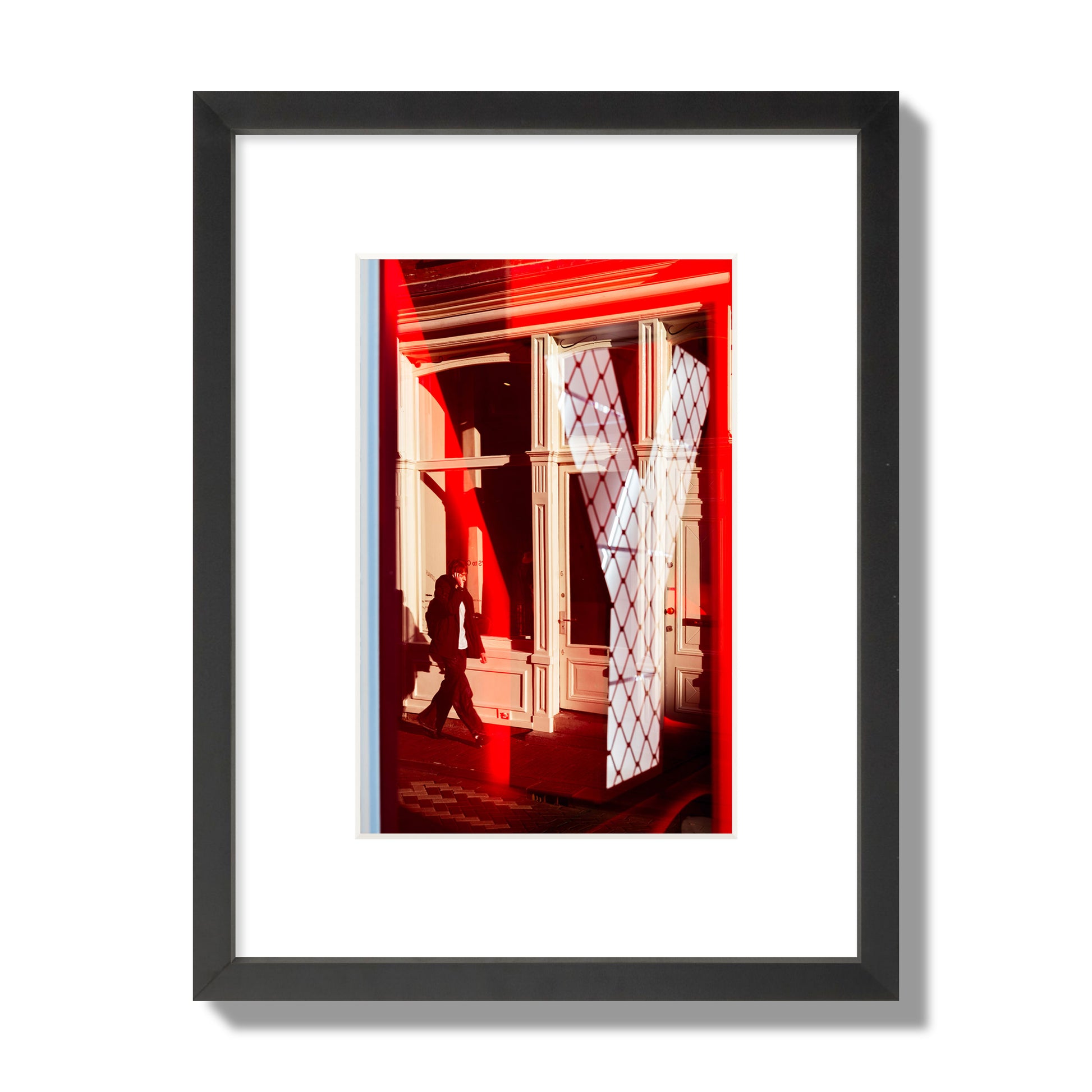 Fine art street photograph of an Amsterdam street scene showing bright red and white reflections of a large letter Y, a man walking, and multiple store fronts. Archival pigment print, small size, black frame.