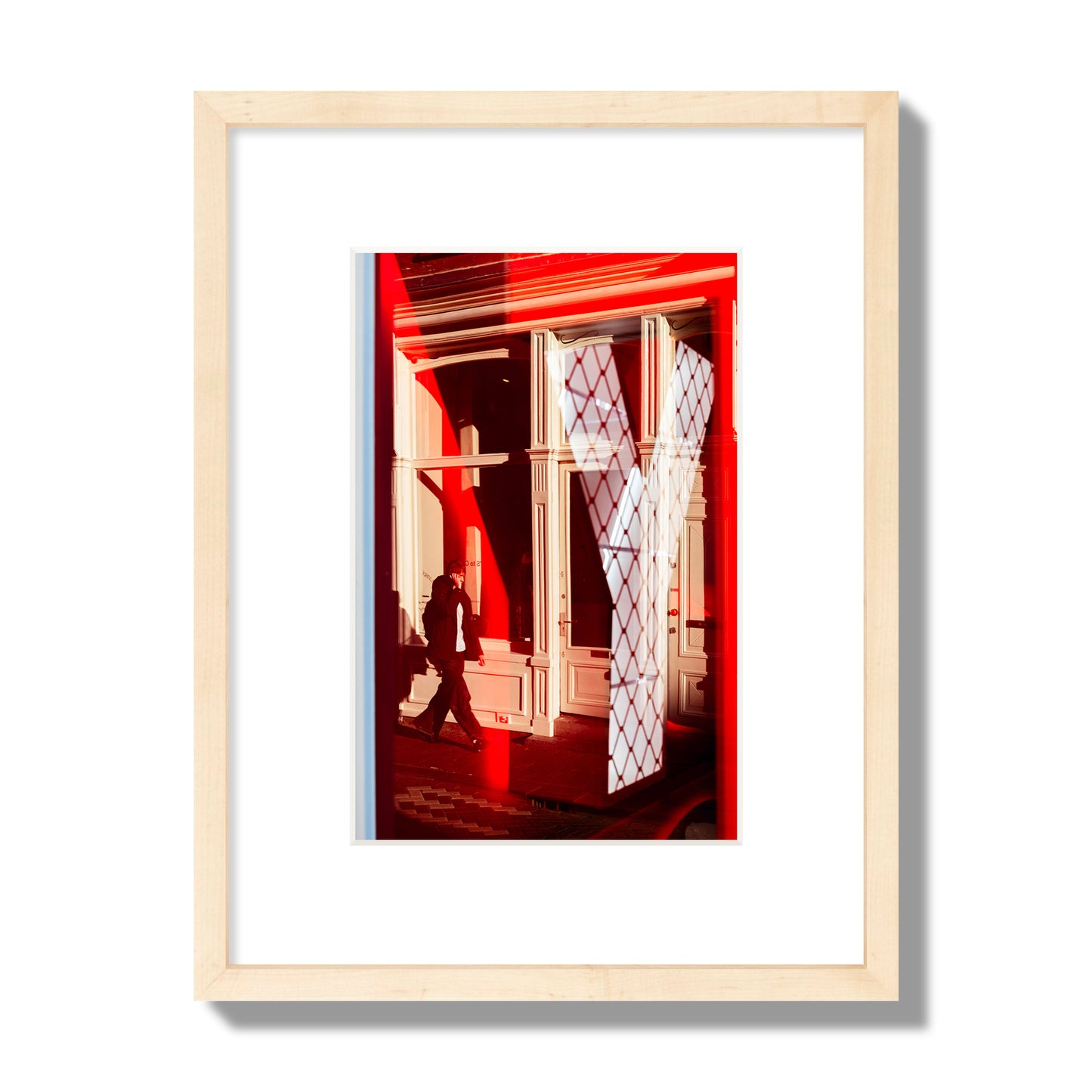 Fine art street photograph of an Amsterdam street scene showing bright red and white reflections of a large letter Y, a man walking, and multiple store fronts. Archival pigment print, small size, natural wood frame.