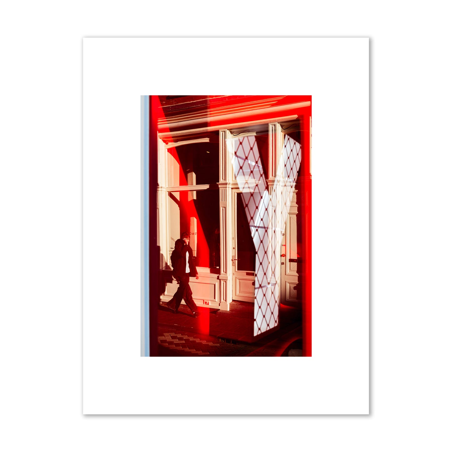 Fine art street photograph of an Amsterdam street scene showing bright red and white reflections of a large letter Y, a man walking, and multiple store fronts. Archival pigment print, small size, unframed.