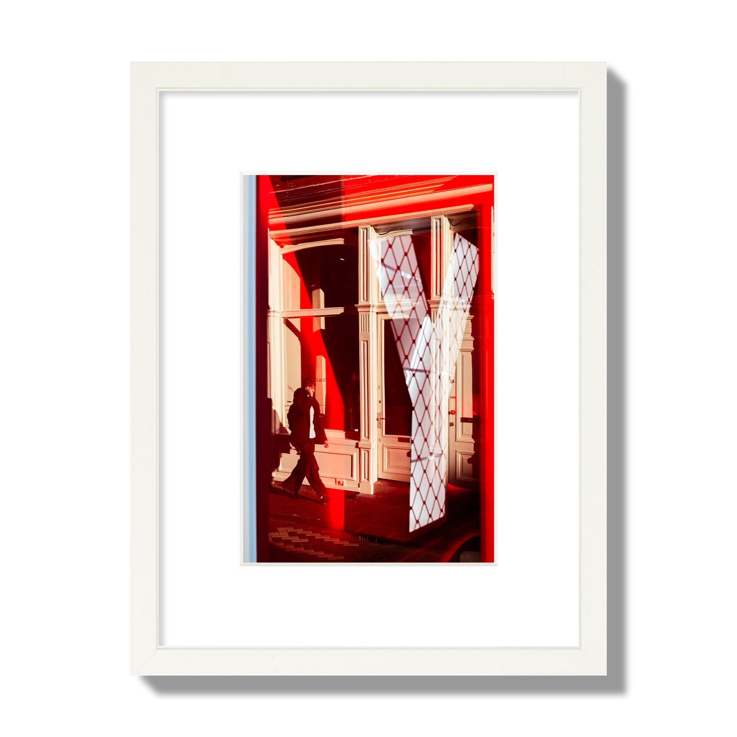 Fine art street photograph of an Amsterdam street scene showing bright red and white reflections of a large letter Y, a man walking, and multiple store fronts. Archival pigment print, small size, white frame.