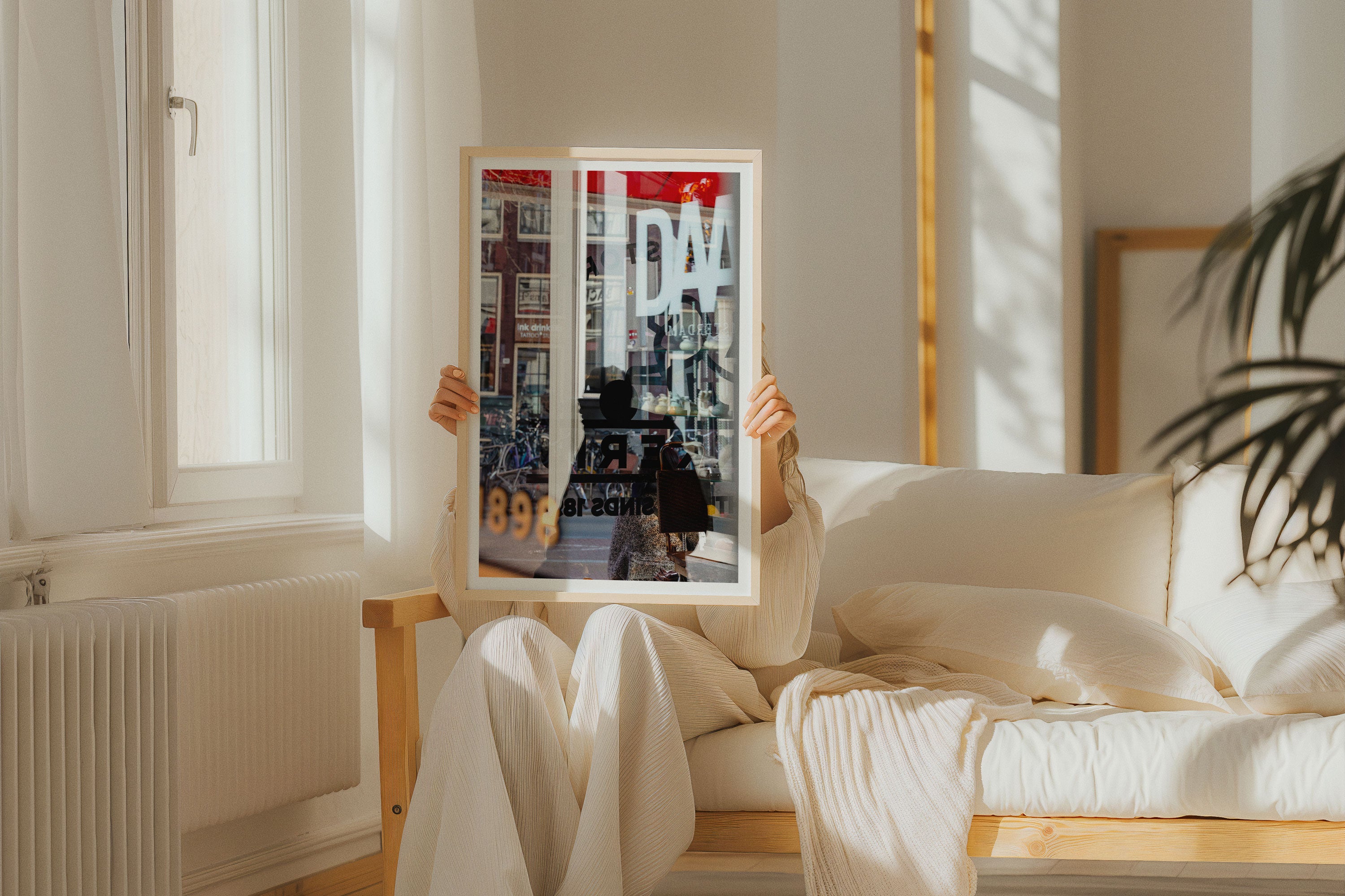 A woman sitting in a contemporary living room holding a framed fine art photograph of a busy Amsterdam street scene.