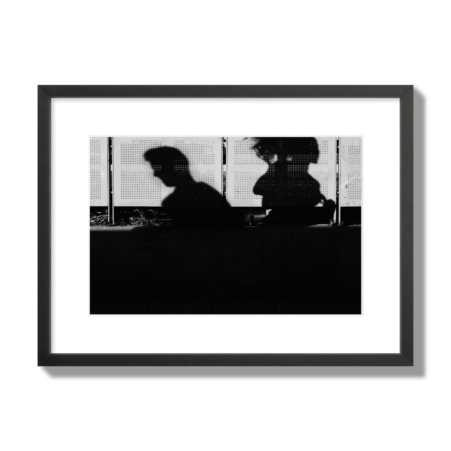 Fine art black and white street photography capturing the silhouettes of two individuals against a wall in Athens Greece, archival pigment print, medium size, black frame