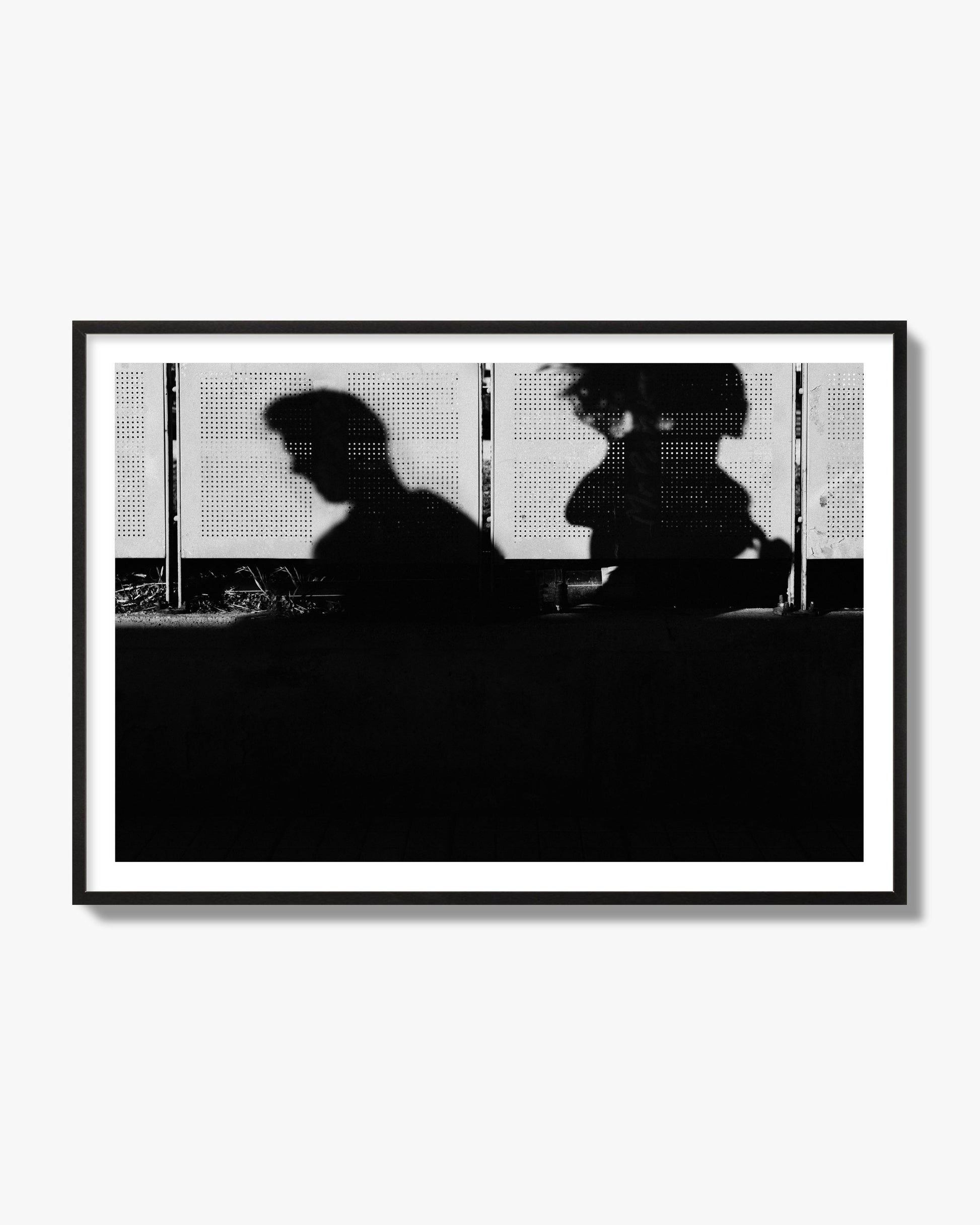 Fine art black and white street photography capturing the silhouettes of two individuals against a wall in Athens Greece, archival pigment print, black frame