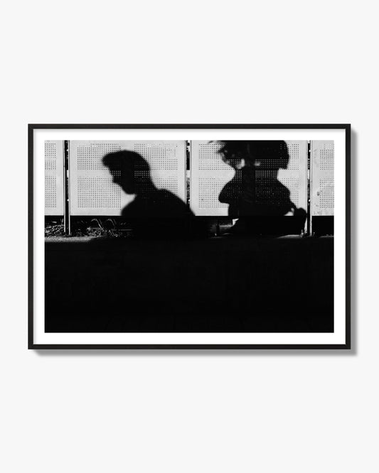 Fine art black and white street photography capturing the silhouettes of two individuals against a wall in Athens Greece, archival pigment print, black frame