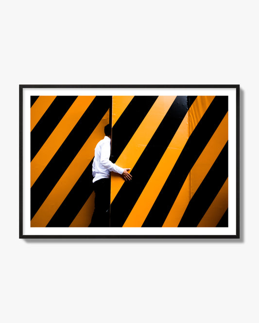 Fine art street photograph of a man opening an orange and black stripped construction door. Archival pigment print, black frame.